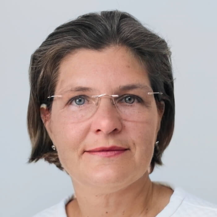 Close-up portrait of a woman with short brown hair and clear glasses, wearing a white top against a light background