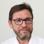 Close-up portrait of a middle-aged man wearing glasses and a white shirt, smiling slightly against a light background
