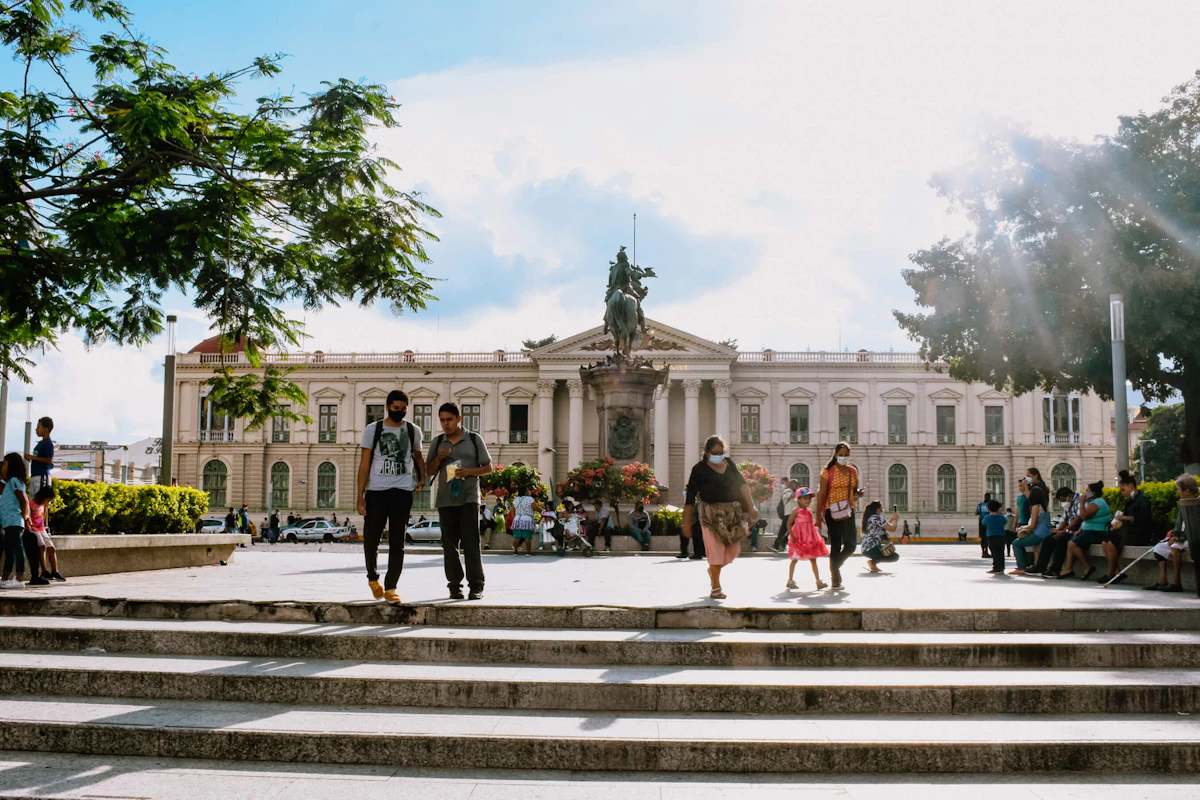 Busy public square in front of a historic building with people walking and sitting, featuring an equestrian statue in the center
