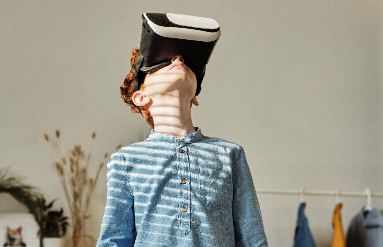 Young boy wearing a virtual reality headset, looking upward in a sunlit room with shadows from window blinds