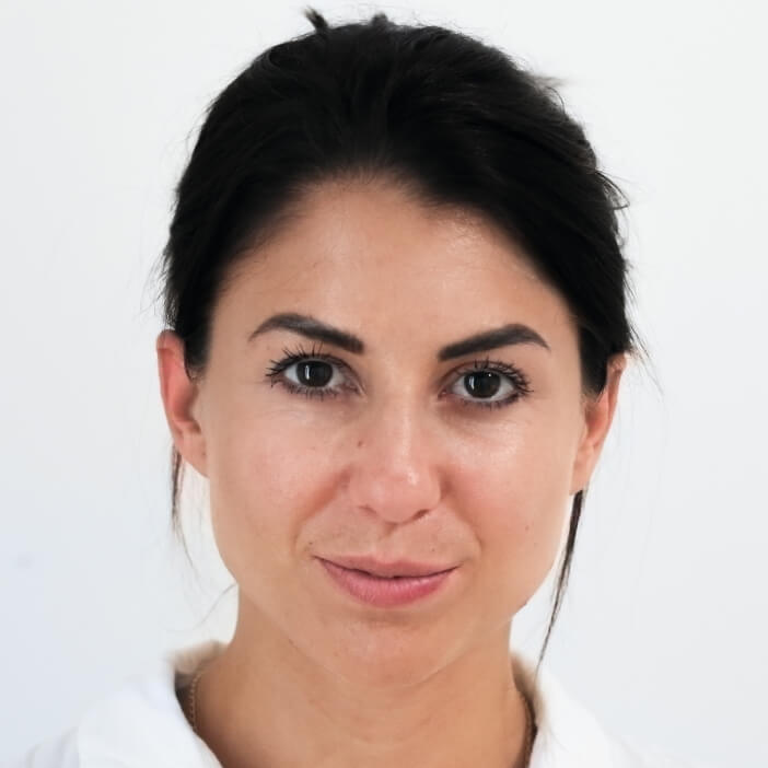 Close-up portrait of a woman with dark hair, natural makeup, and a confident expression against a white background
