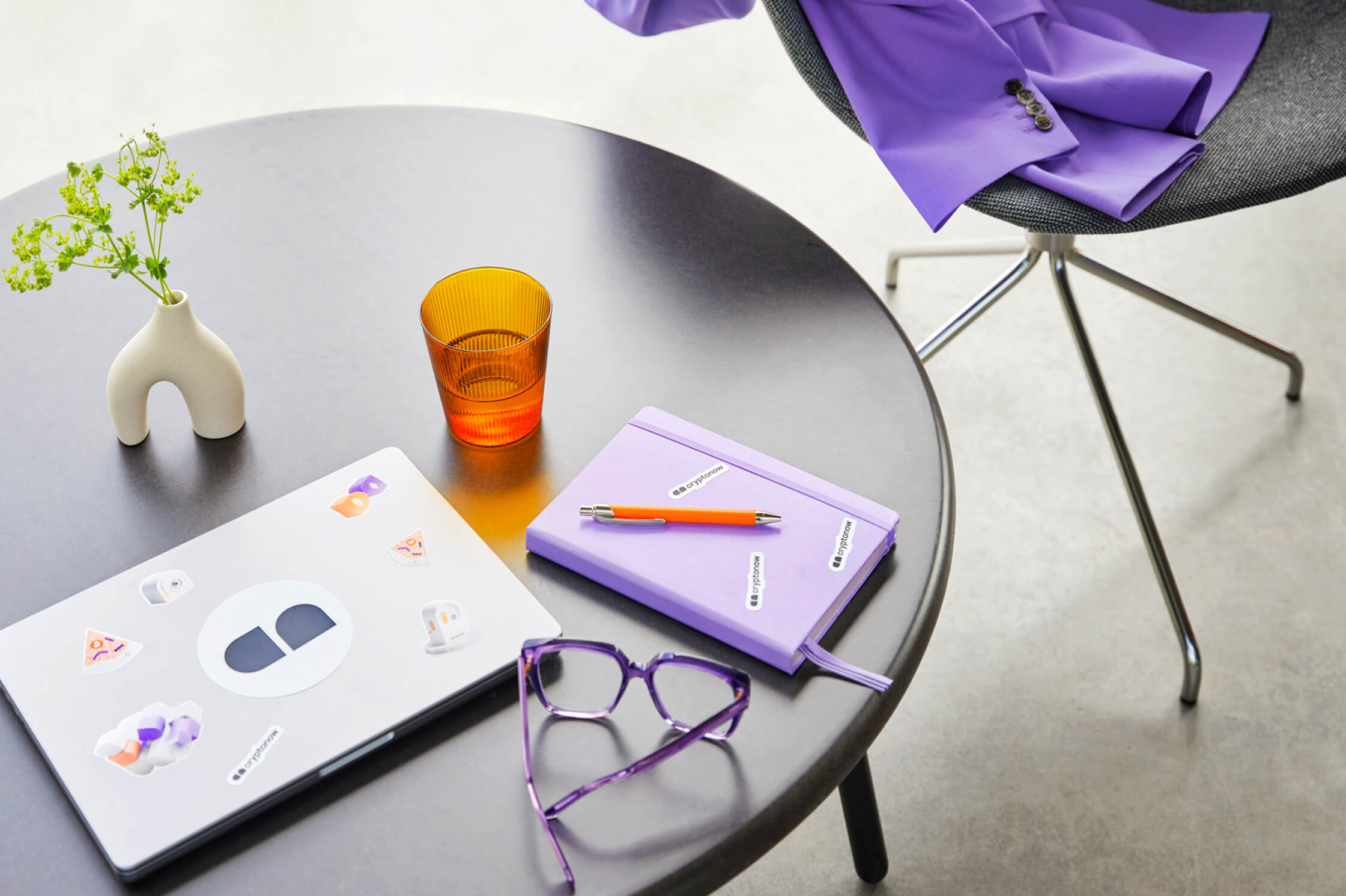 Desk with laptop, purple notebook, glasses and jacket in a modern setting with Cryptonow design colors