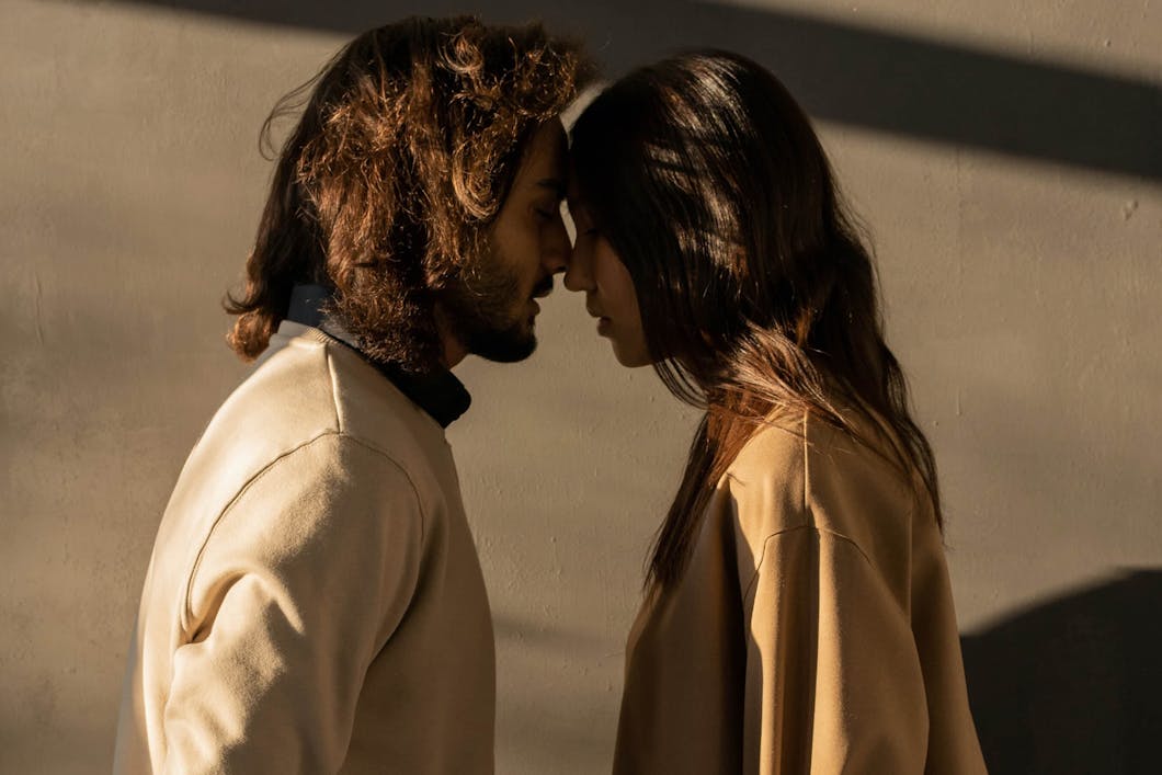 Man and woman standing forehead to forehead in warm sunlight, sharing a calm moment
