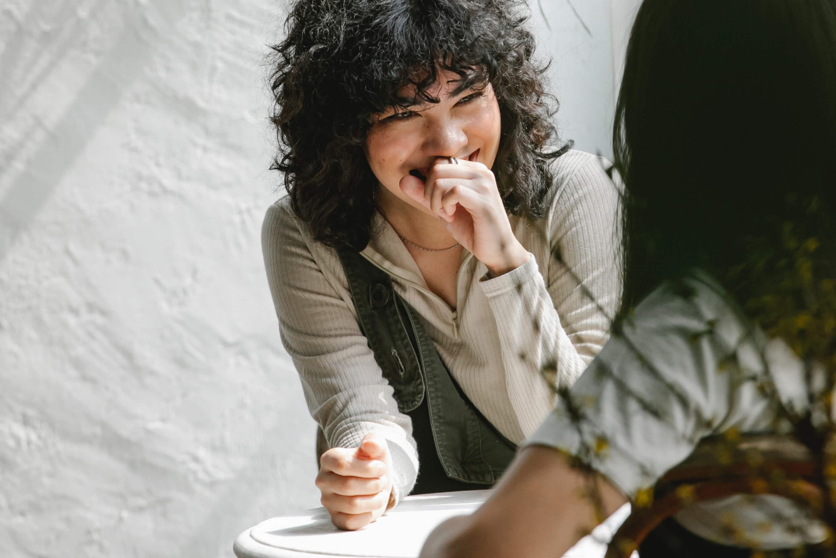 Eine Frau die in einem Kaffee lächelnd zu einer anderen schaut, sie diskutieren das Thema Blockchain.