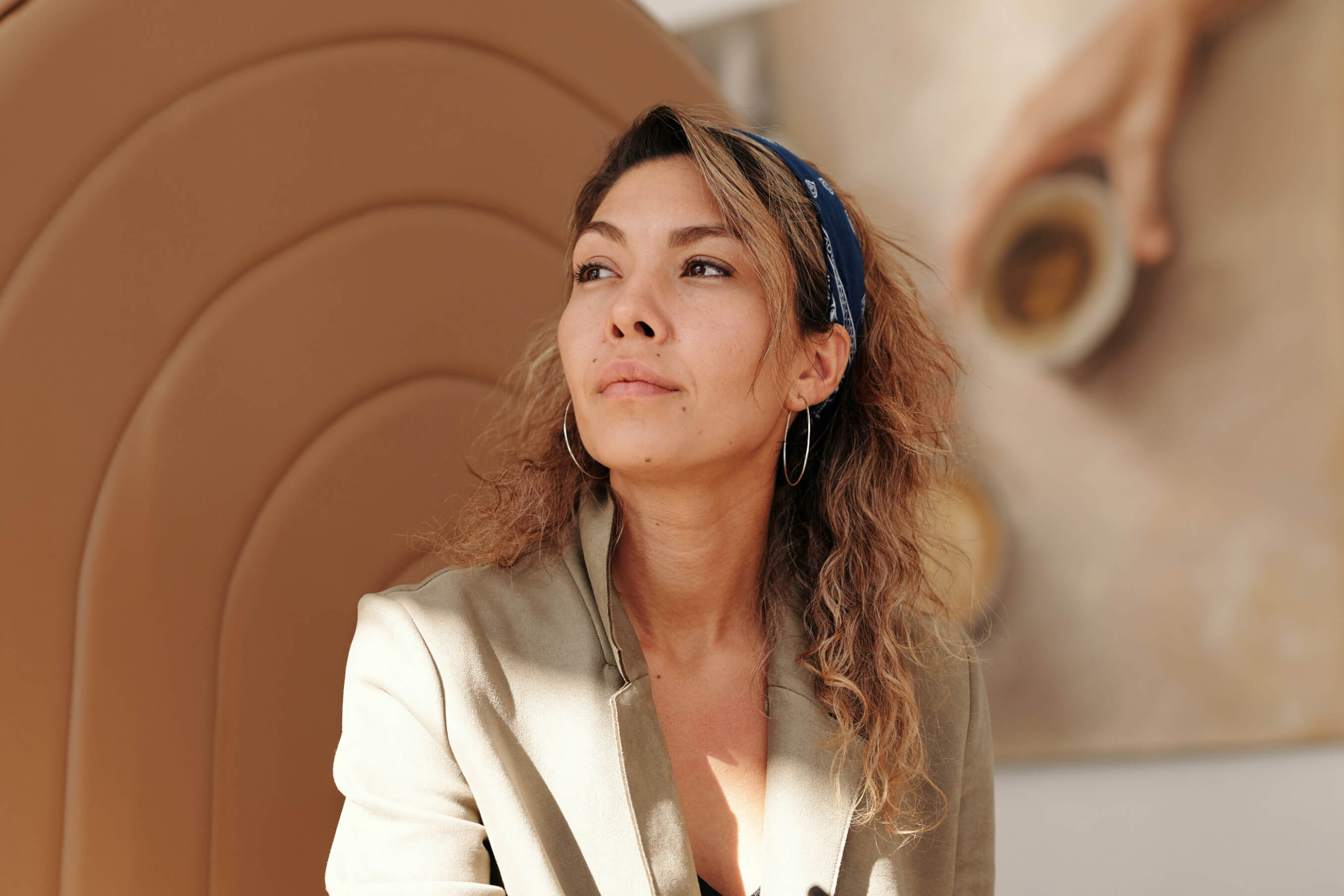 Portrait of a thoughtful woman wearing a blue headband and beige blazer, sitting in warm sunlight