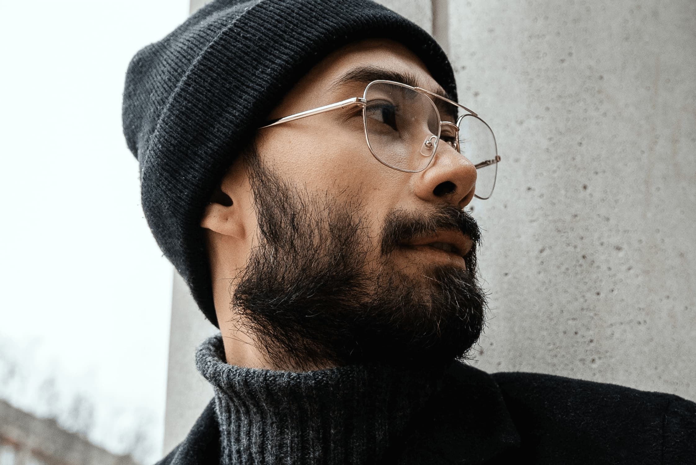 Close-up of a bearded man wearing glasses and a black beanie, looking to the right