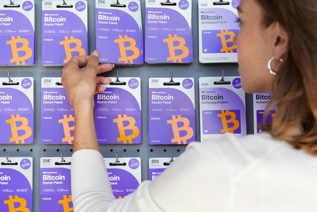 Woman reaching for a purple Bitcoin starter card from a store display filled with cryptocurrency cards