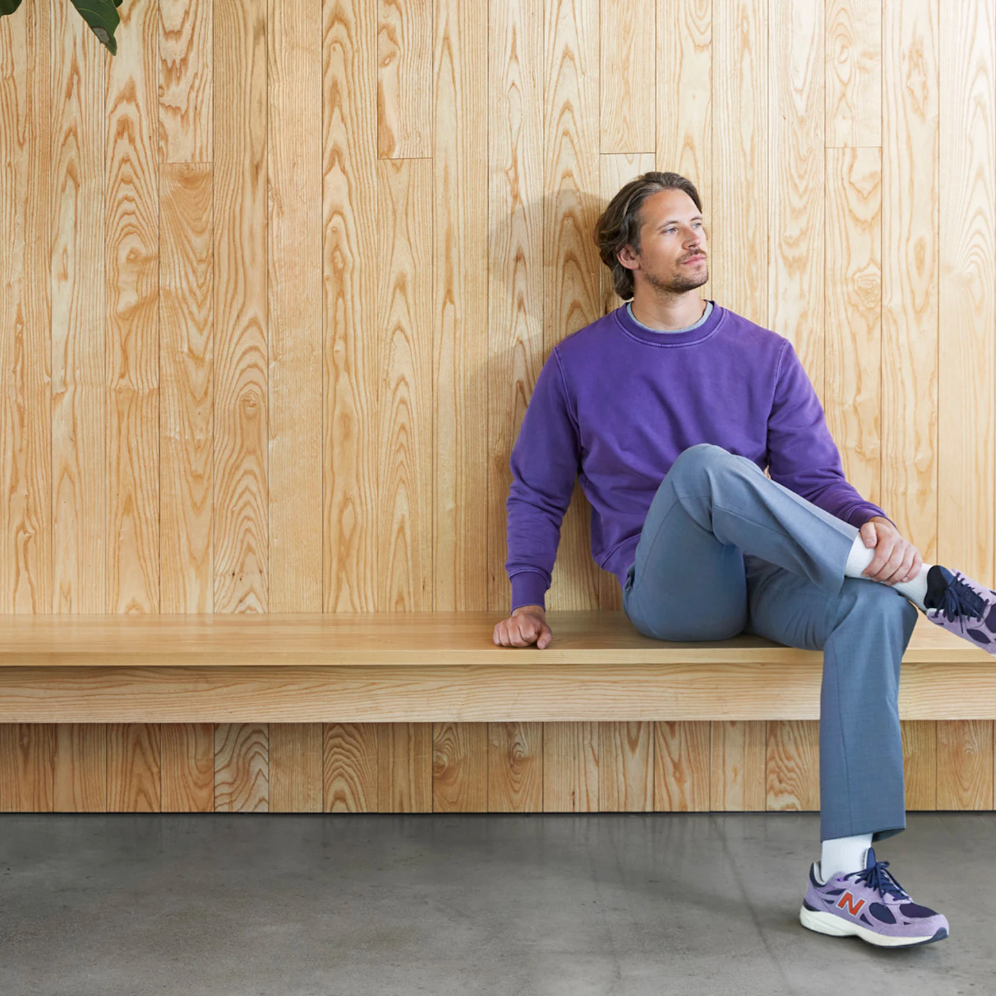 A man in a purple sweater sitting on a bench gazes thoughtfully to the side