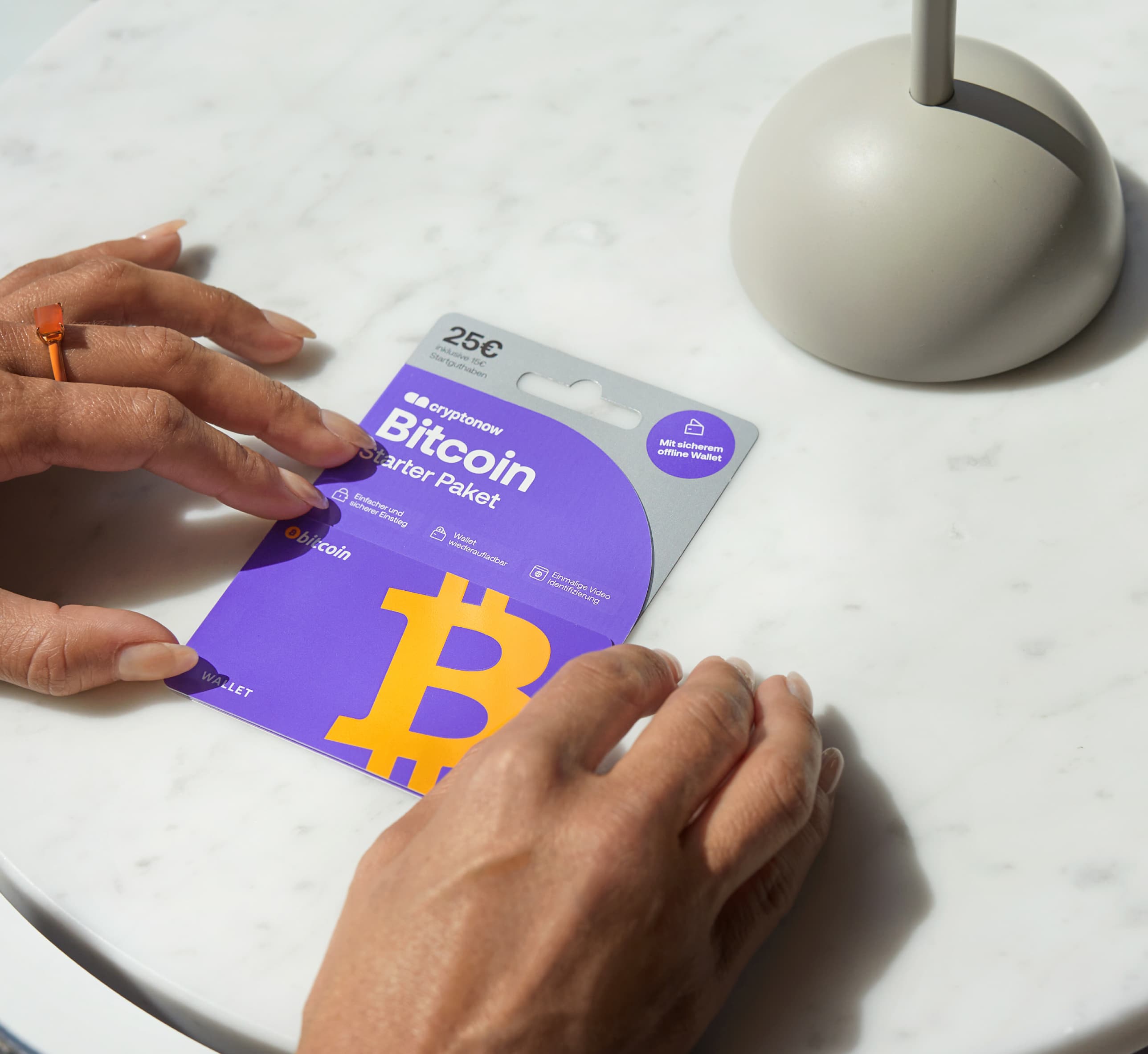 Person holding a purple Cryptonow Bitcoin Starter Pack card worth 25 € on a white marble table