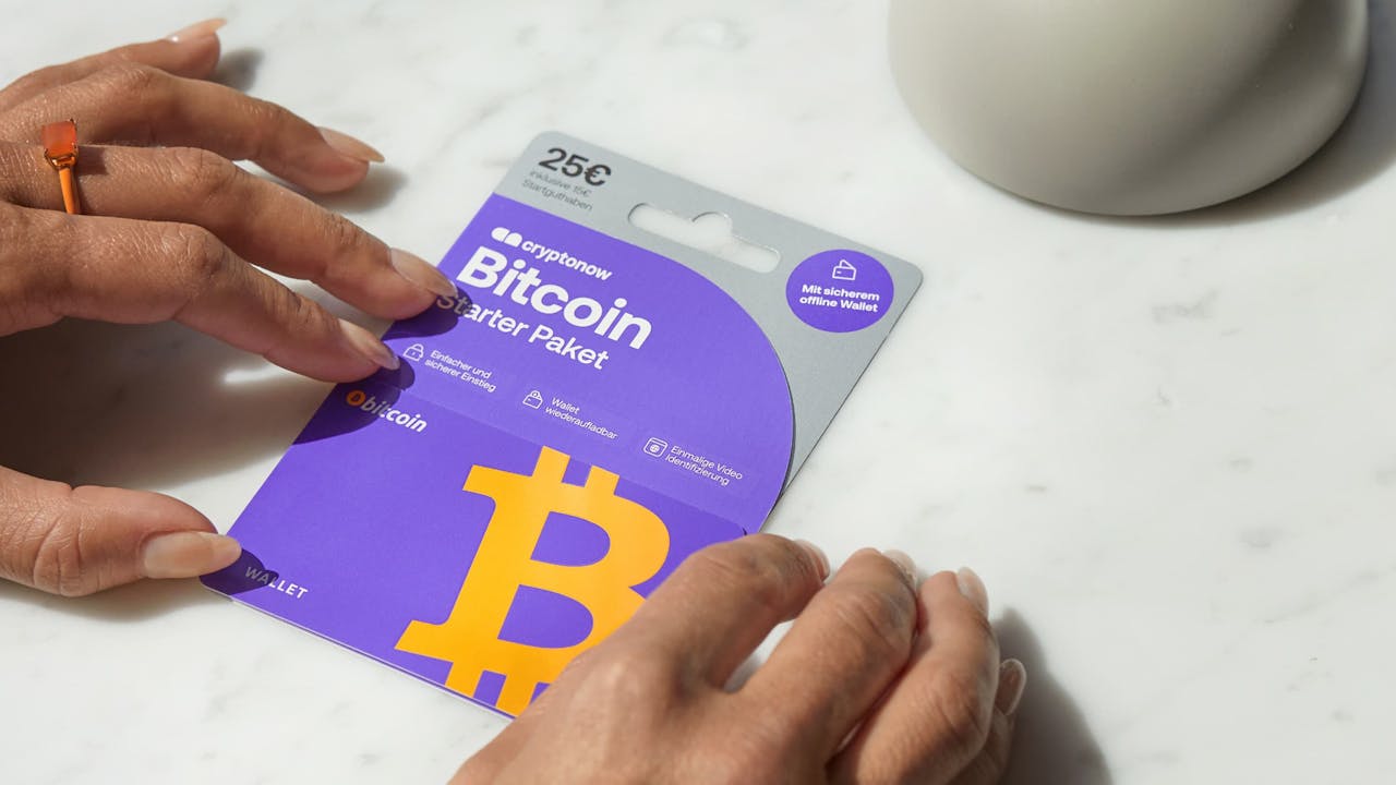 Person holding a purple Cryptonow Bitcoin Starter Pack card worth 25 € on a white marble table