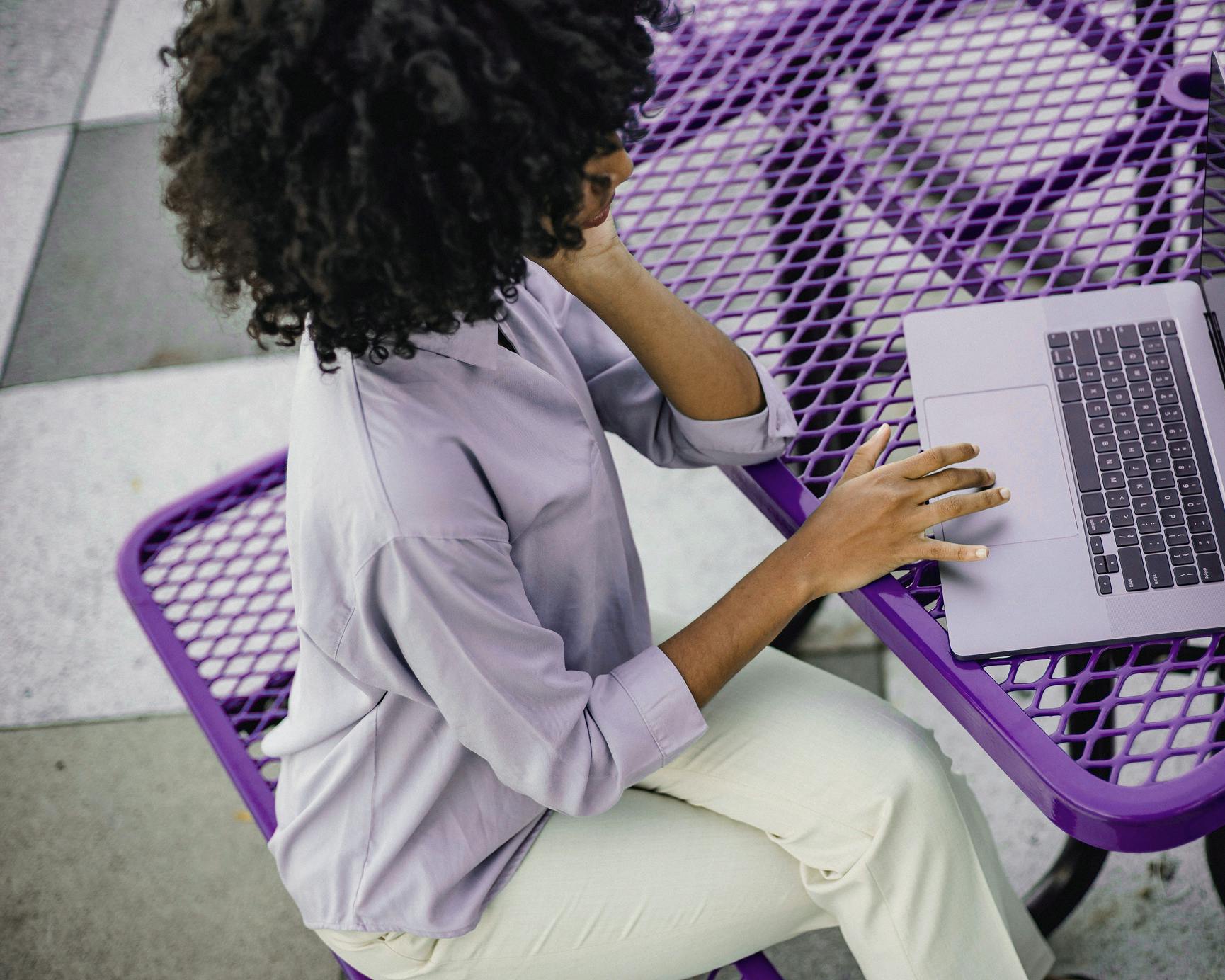 Woman sitting at a purple table, working focused on a laptop outdoors