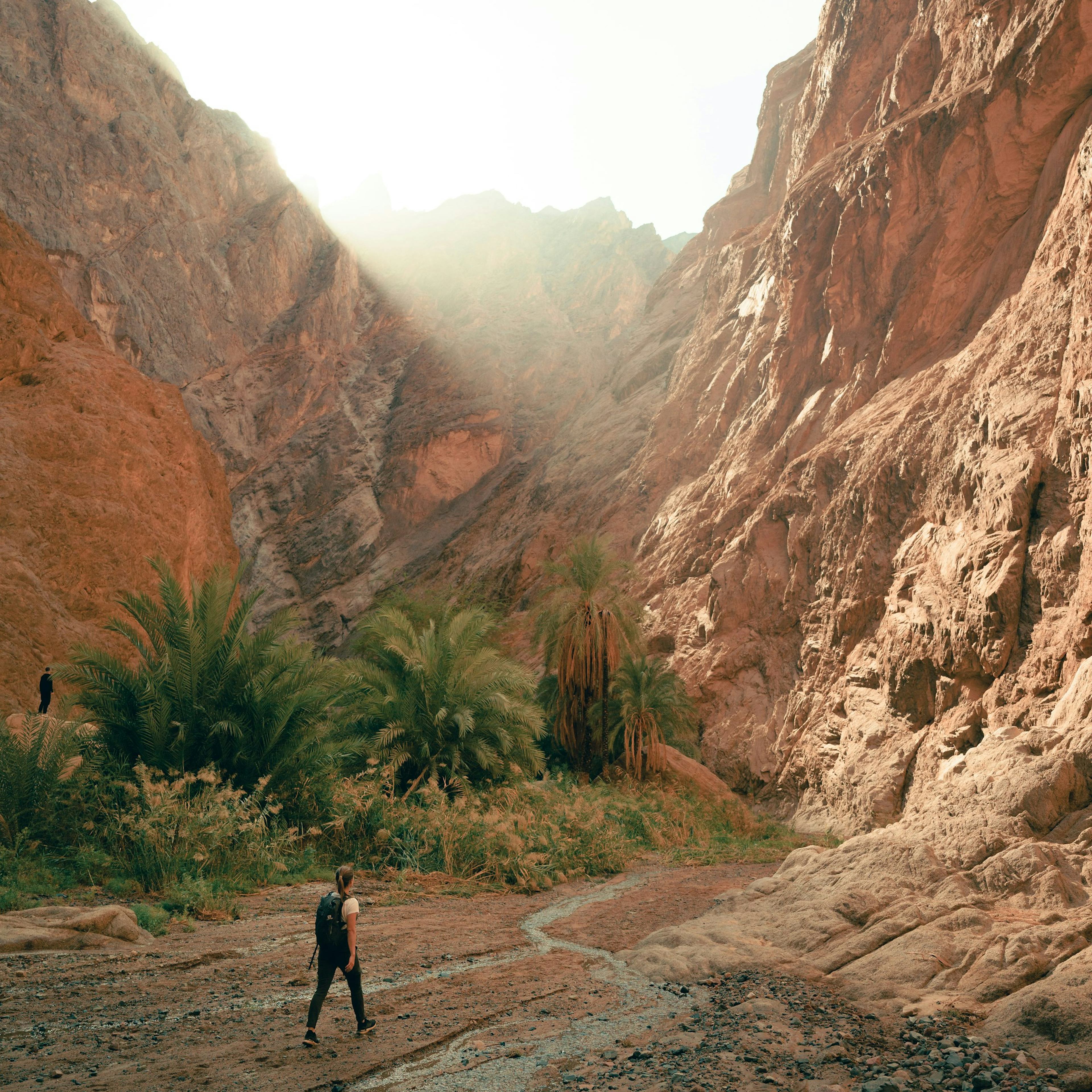 a man walking down a dirt road next to a mountain