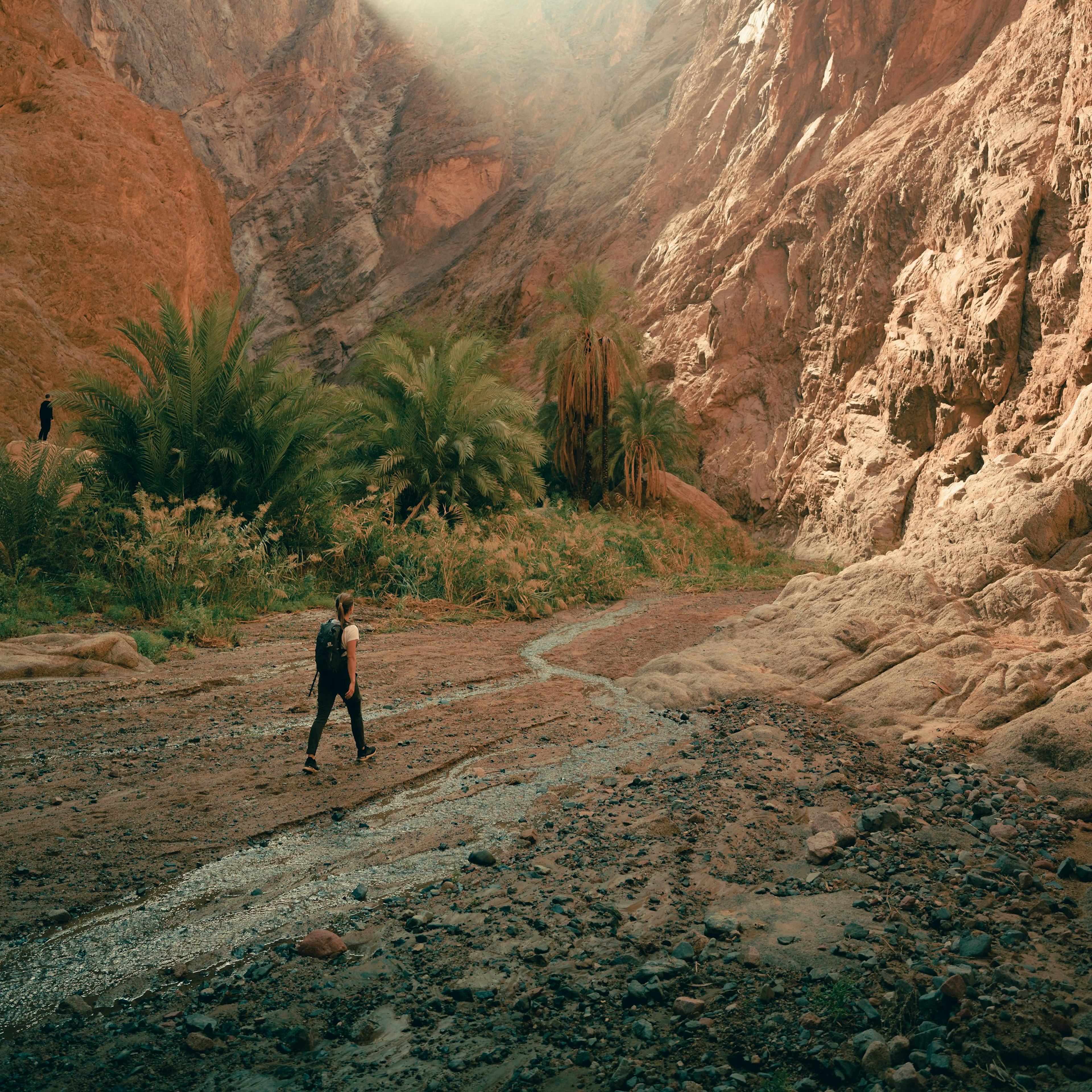 a man walking down a dirt road next to a mountain