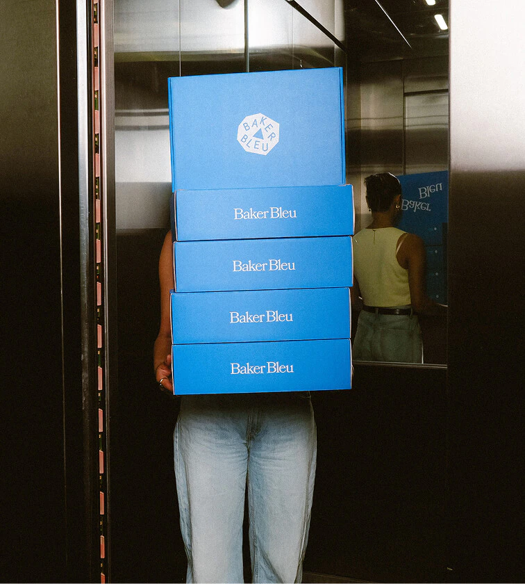 Stack of Baker Bleu catering boxes being carried for delivery, ready for office catering, events and special occasions.