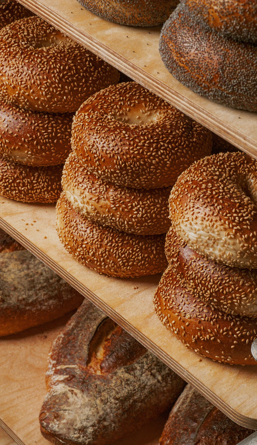 Freshly baked sesame bagels displayed on wooden bakery shelves at Baker Bleu, handcrafted daily and available for catering.