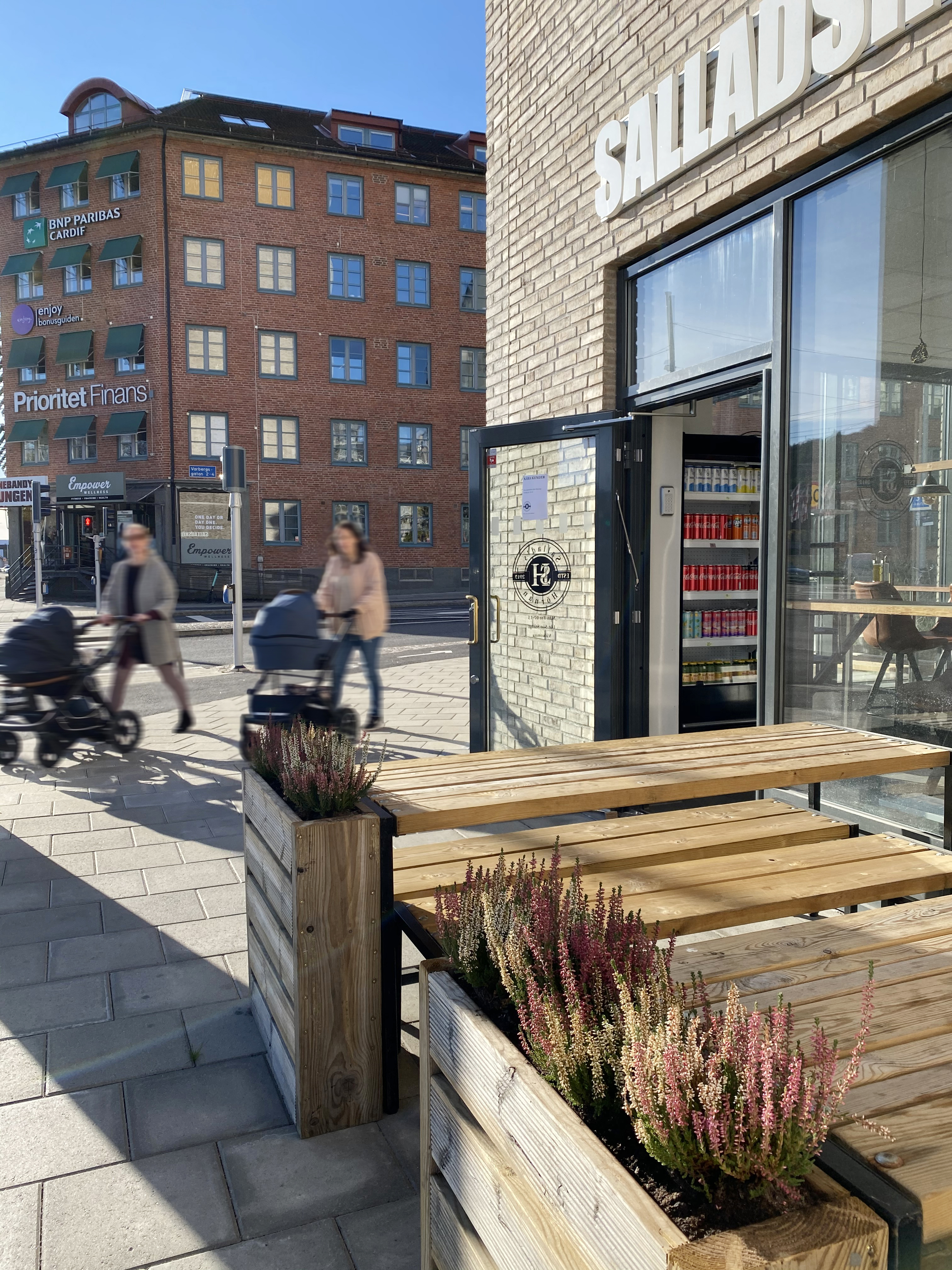 Personer med barnvagnar passerar framför vår fastighet i Krokslätt på Mölndalsvägen med café i förgrunden