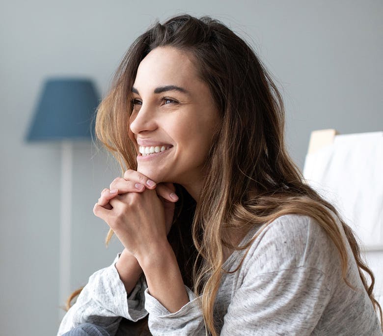 woman smiling while sitting on couch with her hands under her chin
