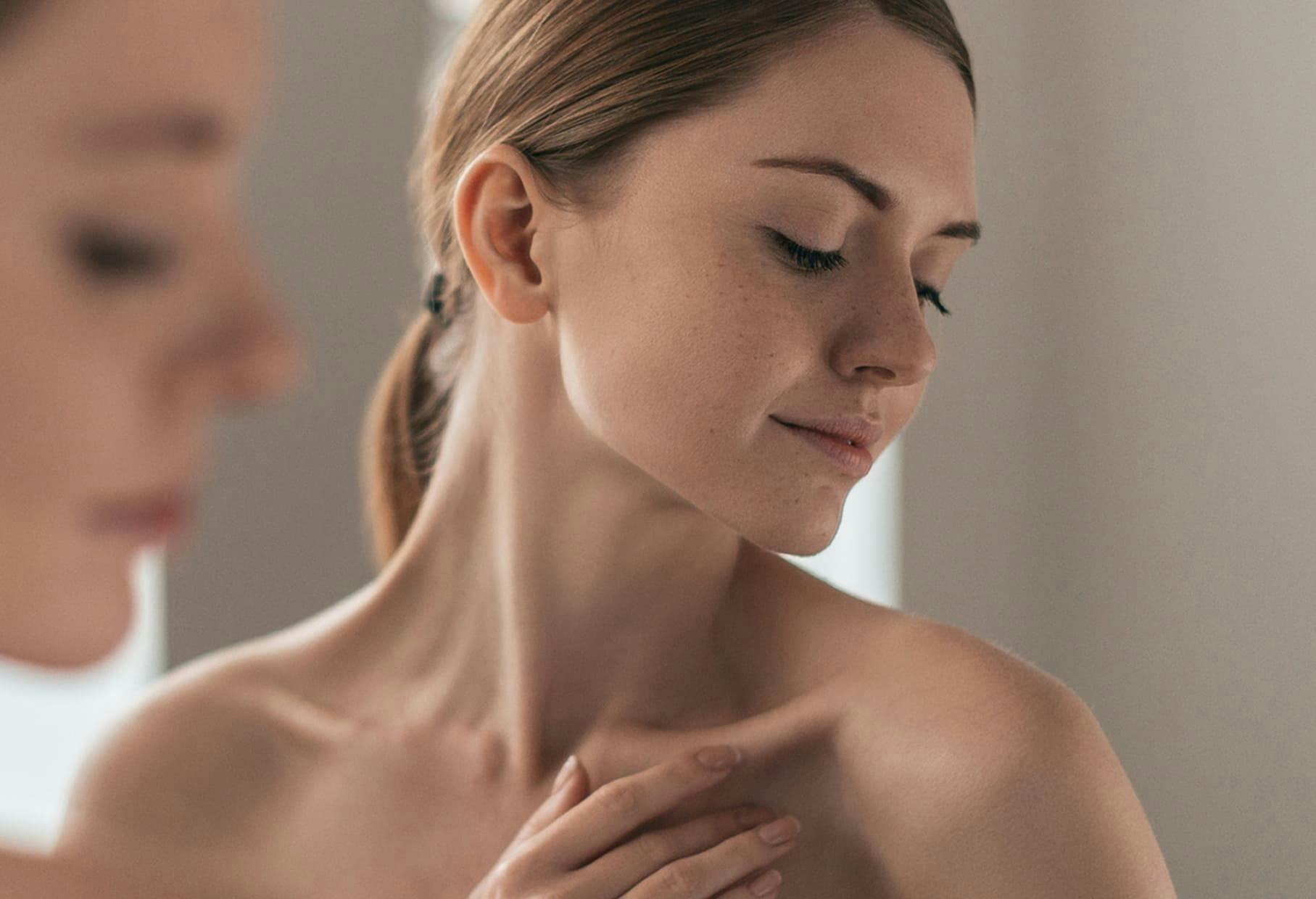 woman in mirror looking downwards and touching her collarbone