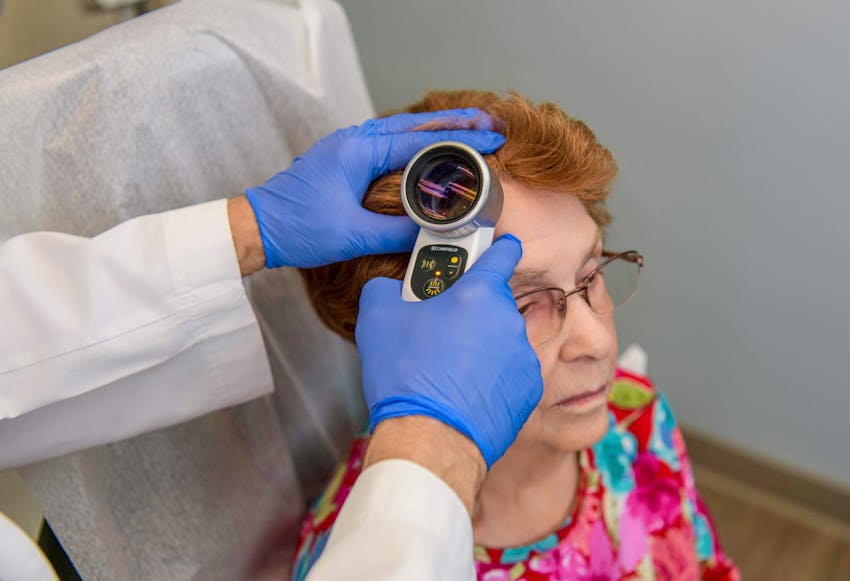 female patient sitting while Abdul looking at her scalp with magnifying glass