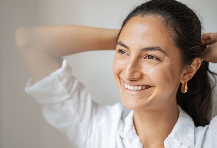 woman smiling as she ties her hair back into a ponytail