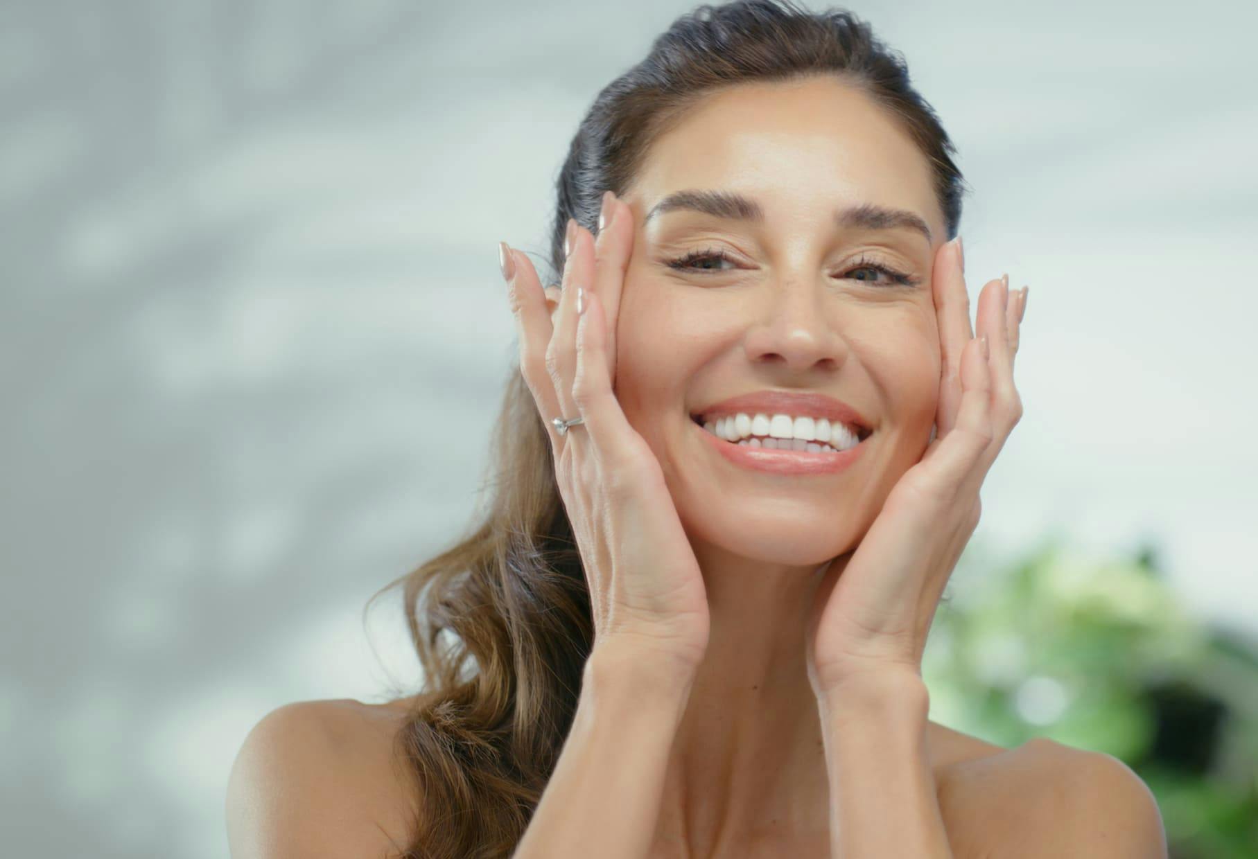 woman looking in mirror, smiling and touching her temples with her fingers