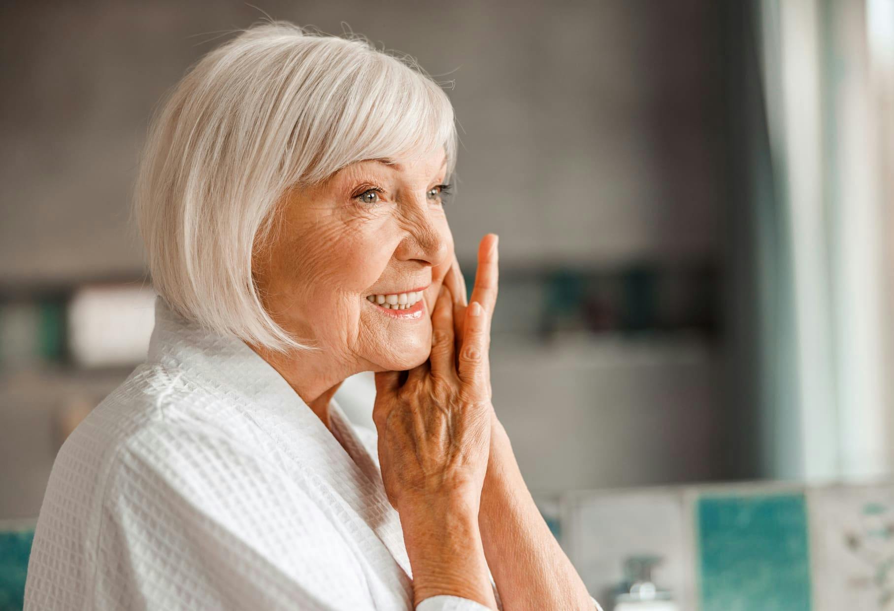older woman smiling with her hands near her face