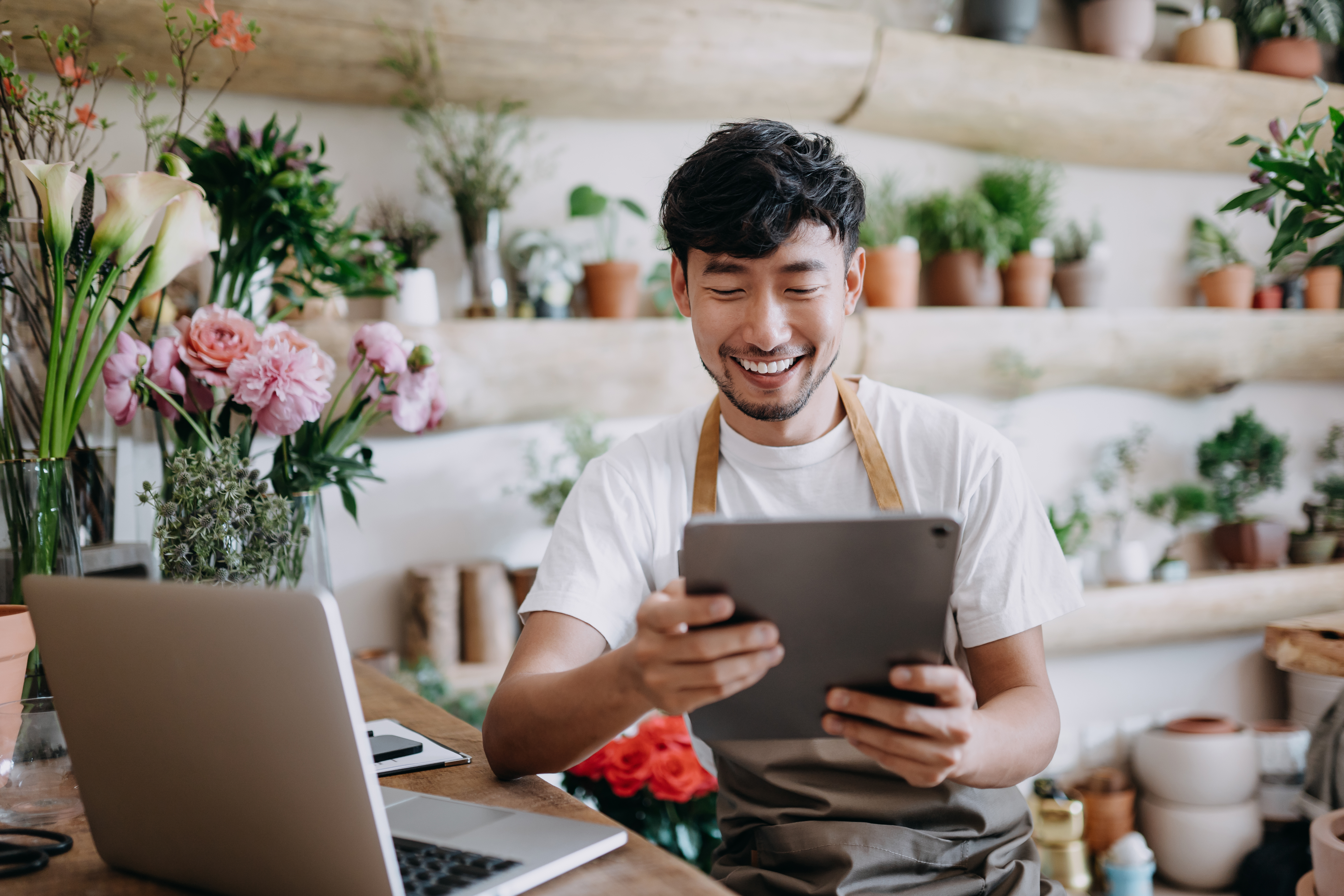 Business owner in flower shop handling monthly banking on a tablet.