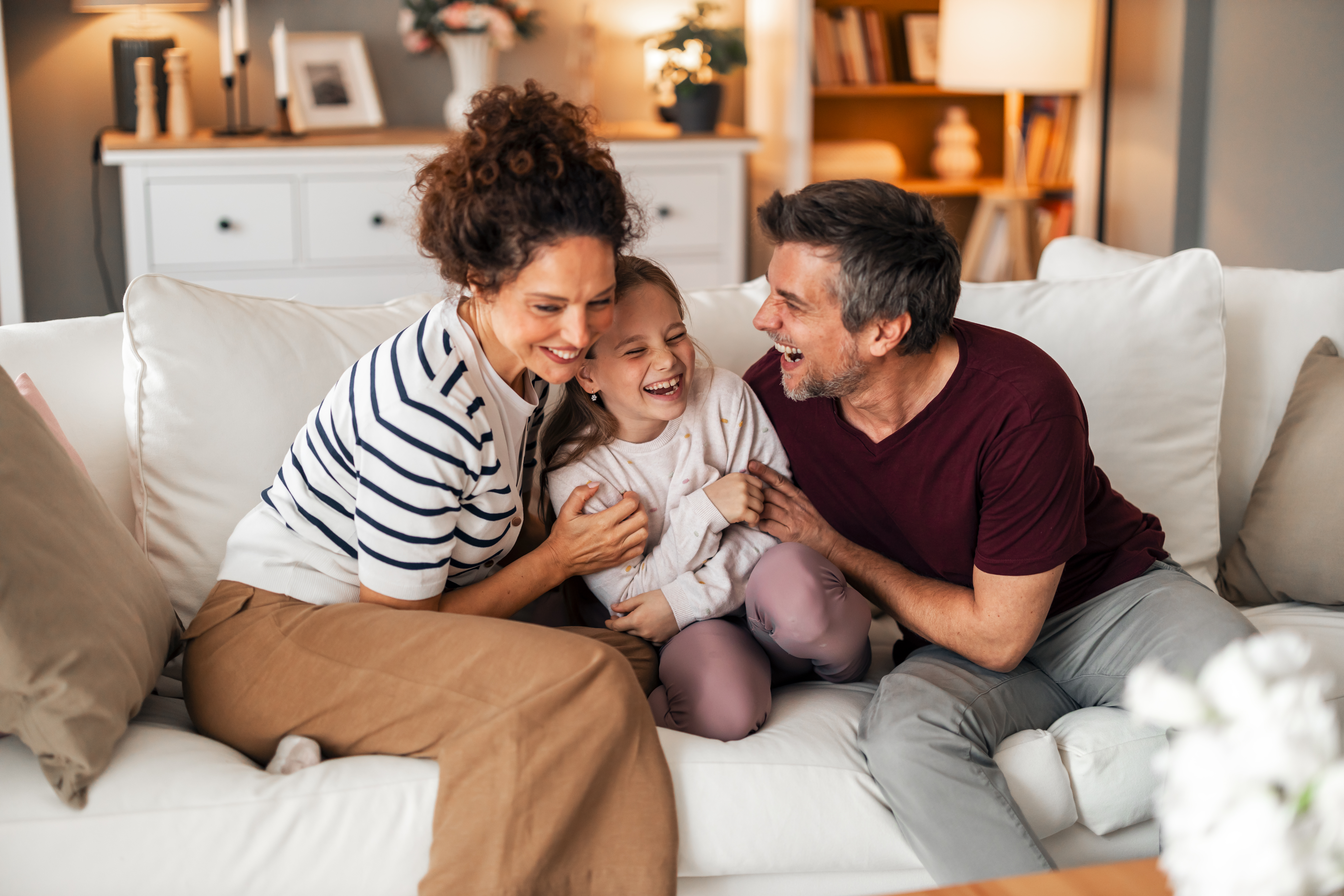 Middle aged parents with young daughter on sofa, laughing.