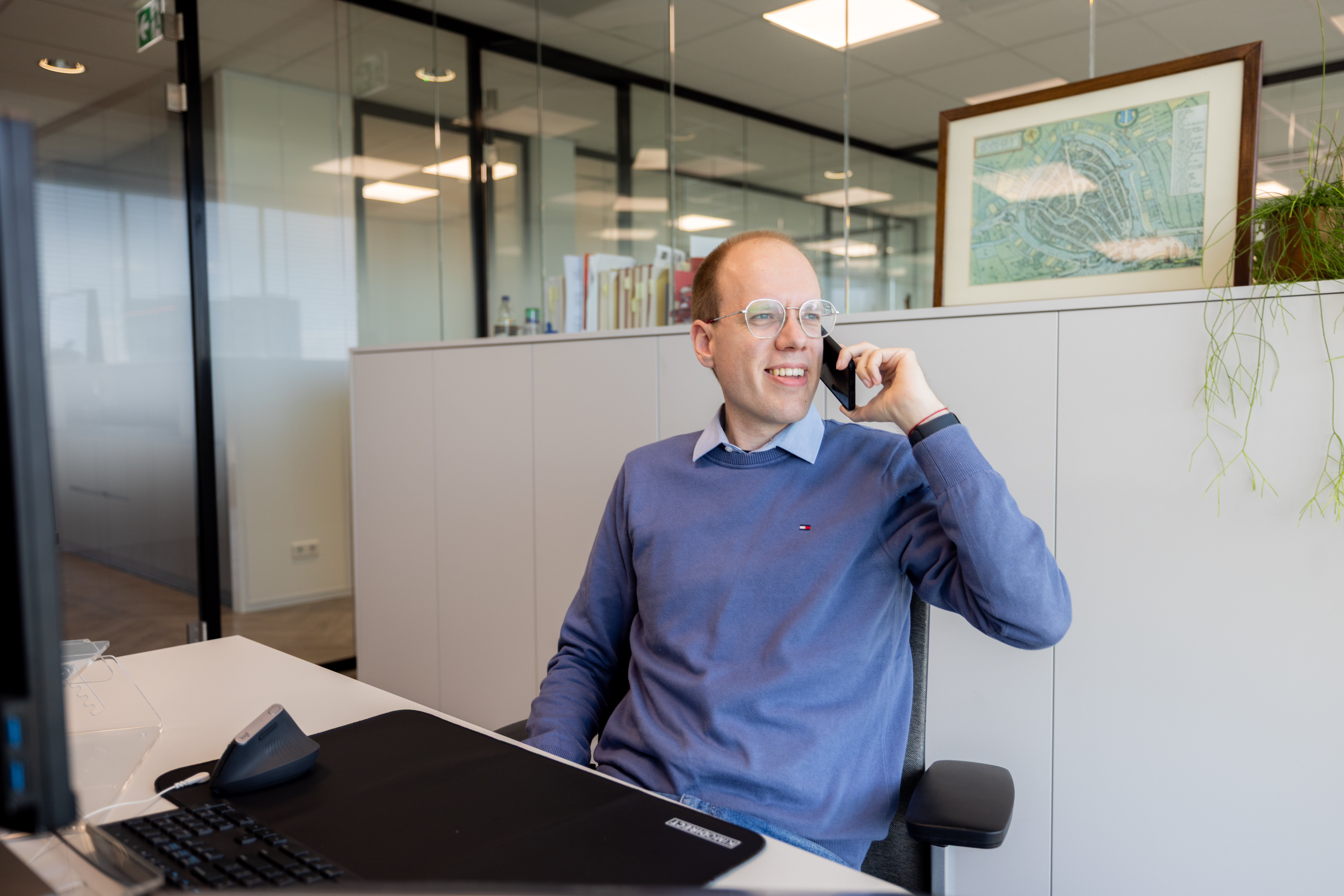 Persoon met een telefoon in de hand, zittend achter een bureau.