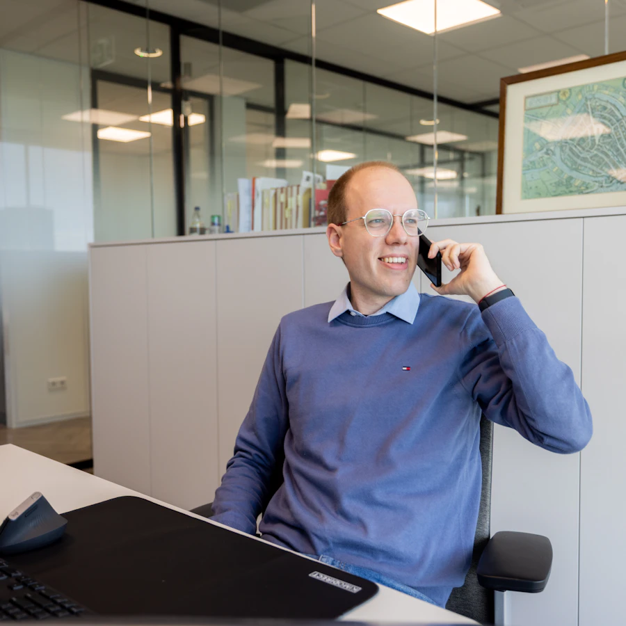 Persoon met een telefoon in de hand, zittend achter een bureau.