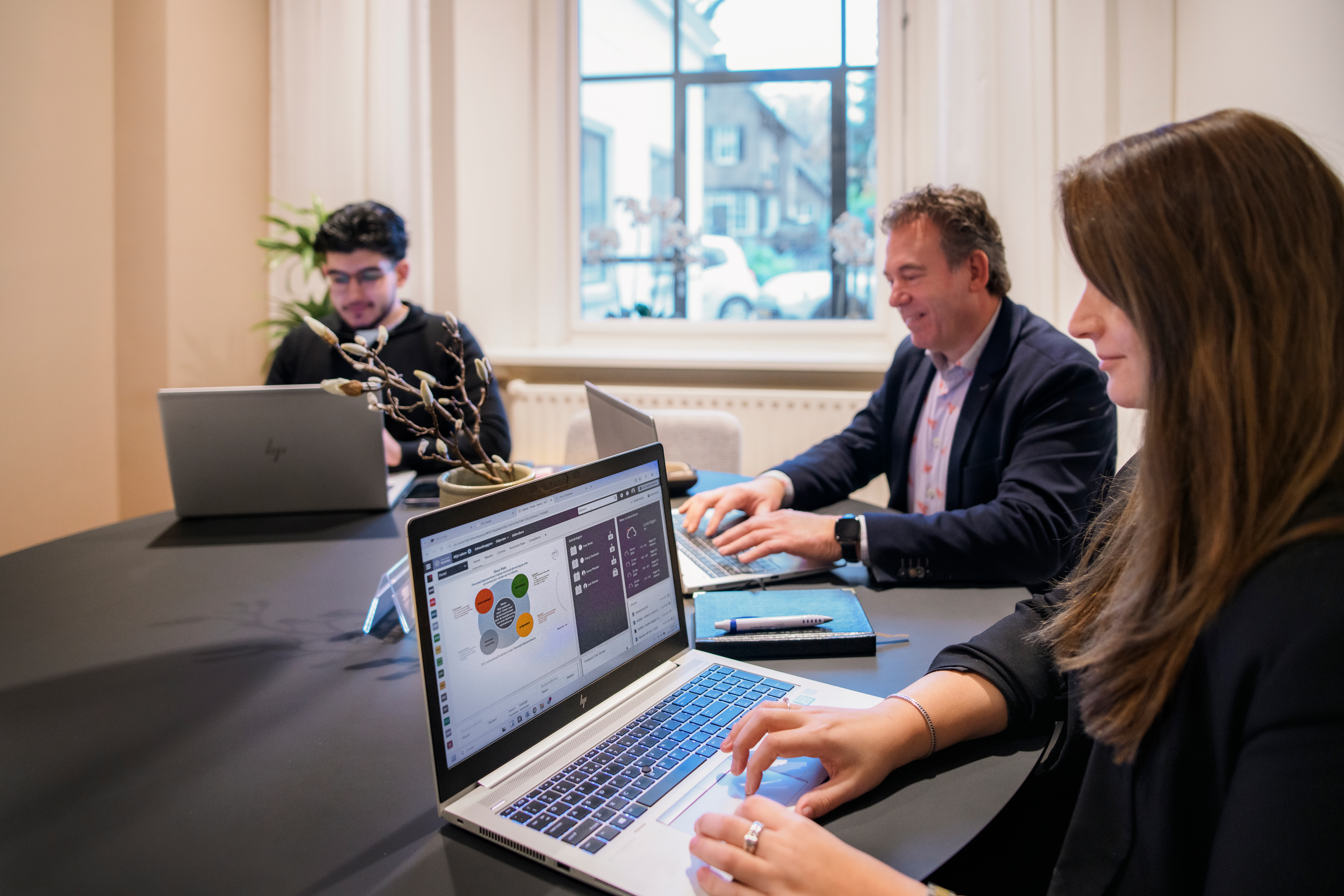 Drie personen aan een tafel, ze zijn aan het werk achter hun laptops.