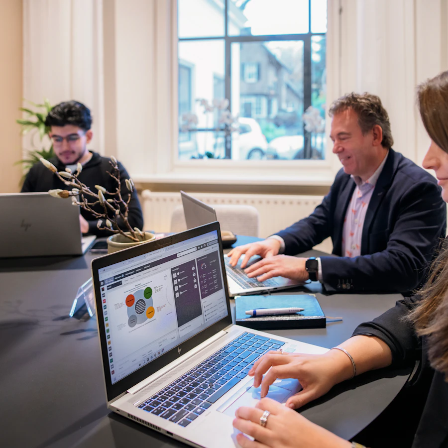 Drie personen aan een tafel, ze zijn aan het werk achter hun laptops.