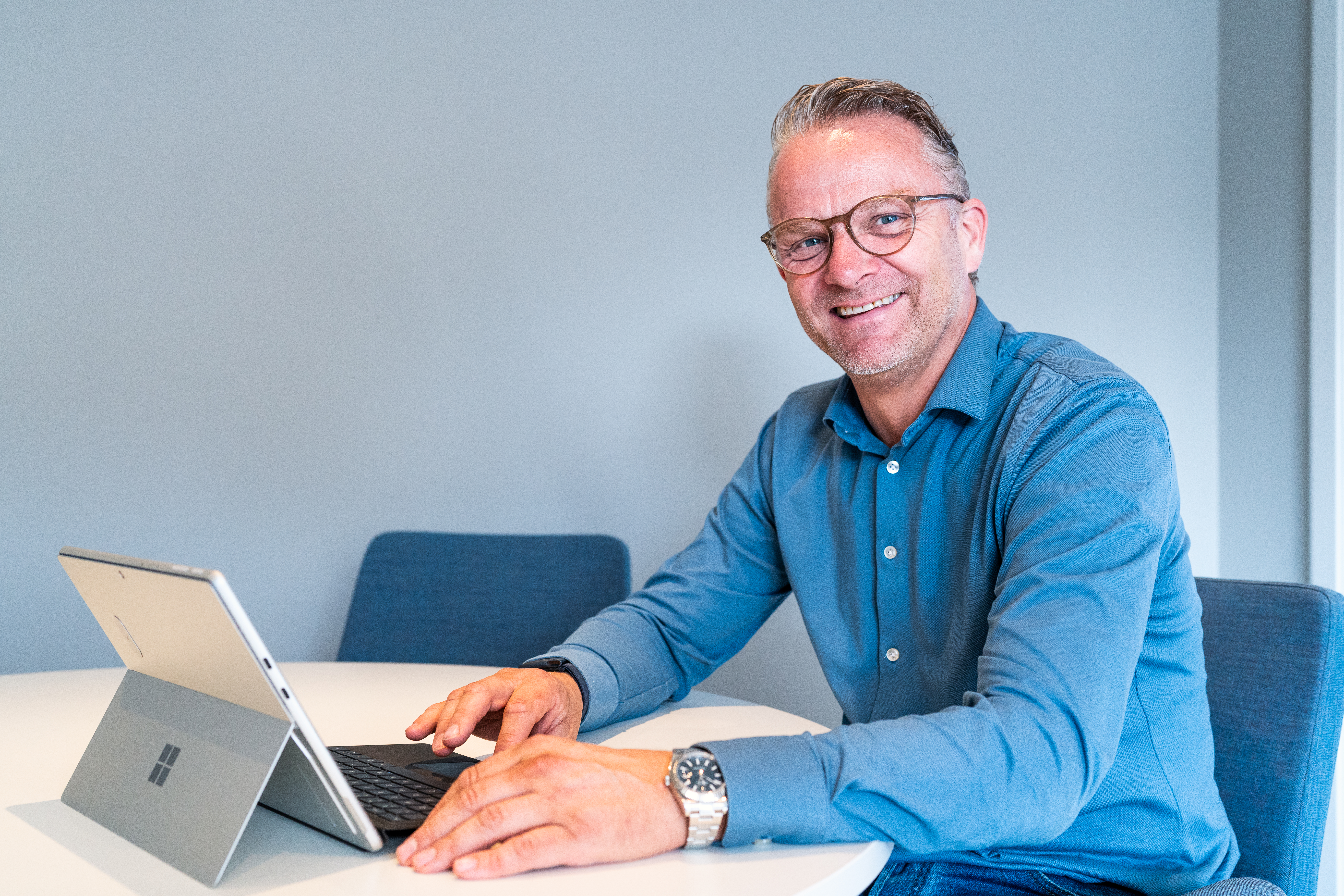 Persoon zit achter een laptop en kijkt lachend de camera in.