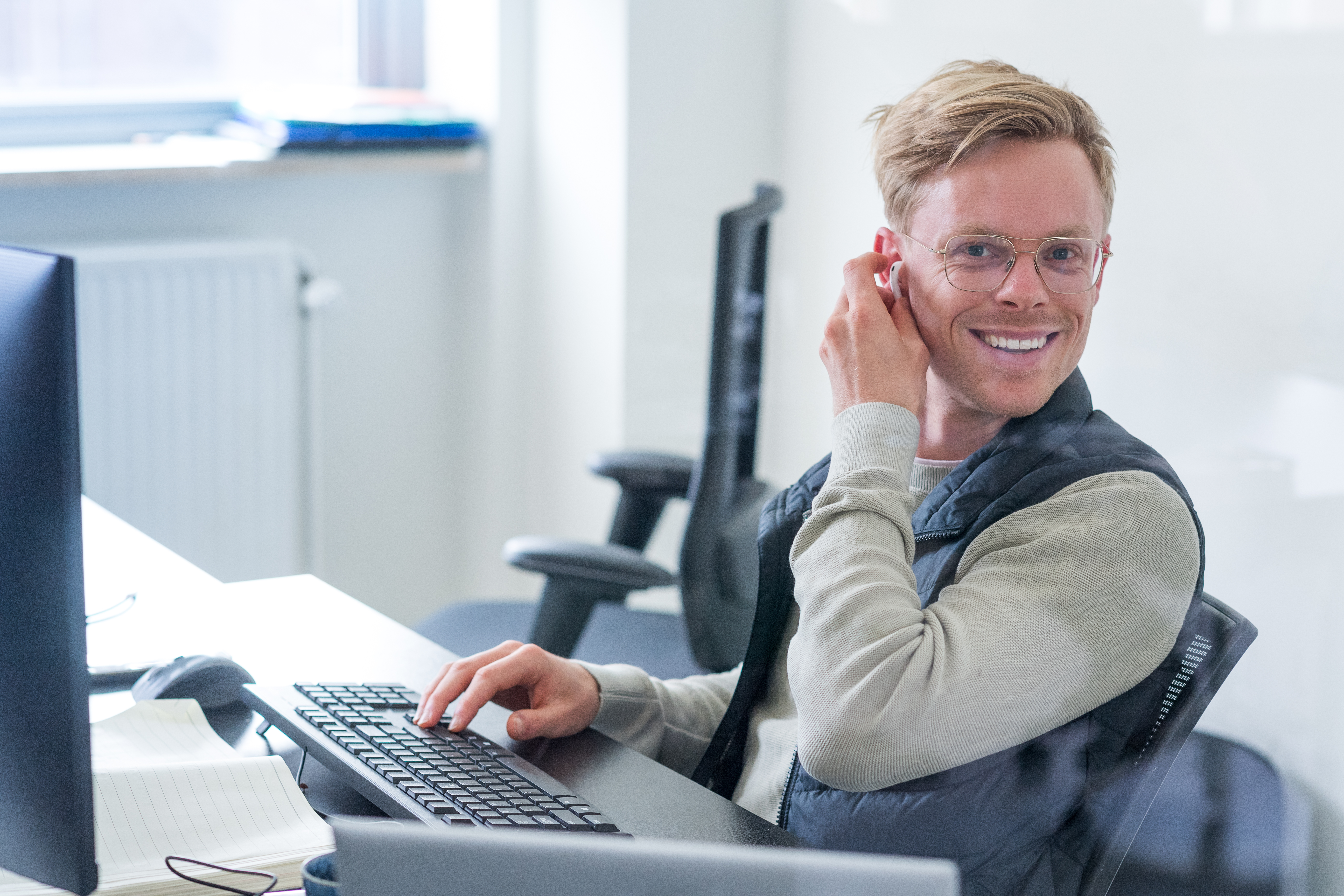 Persoon achter een bureau, kijkt de camera in.