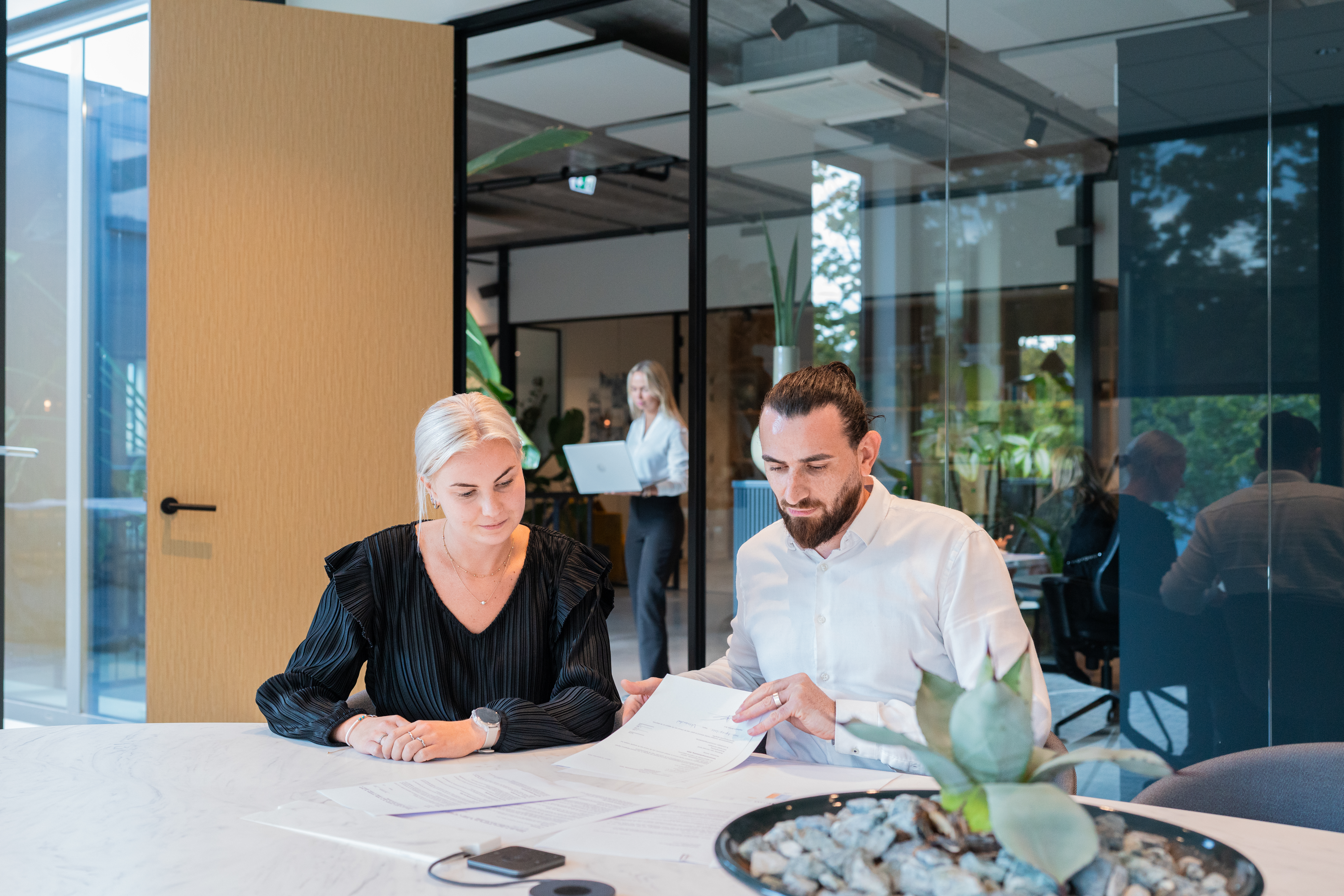 Twee personen zitten samen aan tafel, ze bekijken papieren die voor hen liggen.