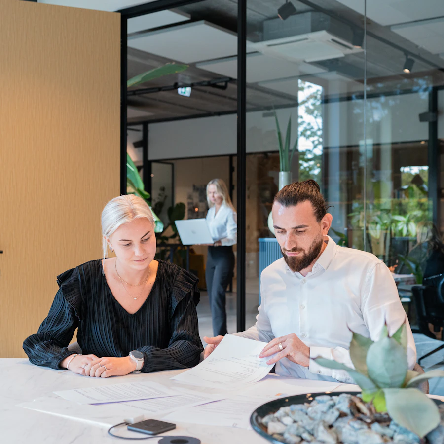 Twee personen zitten samen aan tafel, ze bekijken papieren die voor hen liggen.