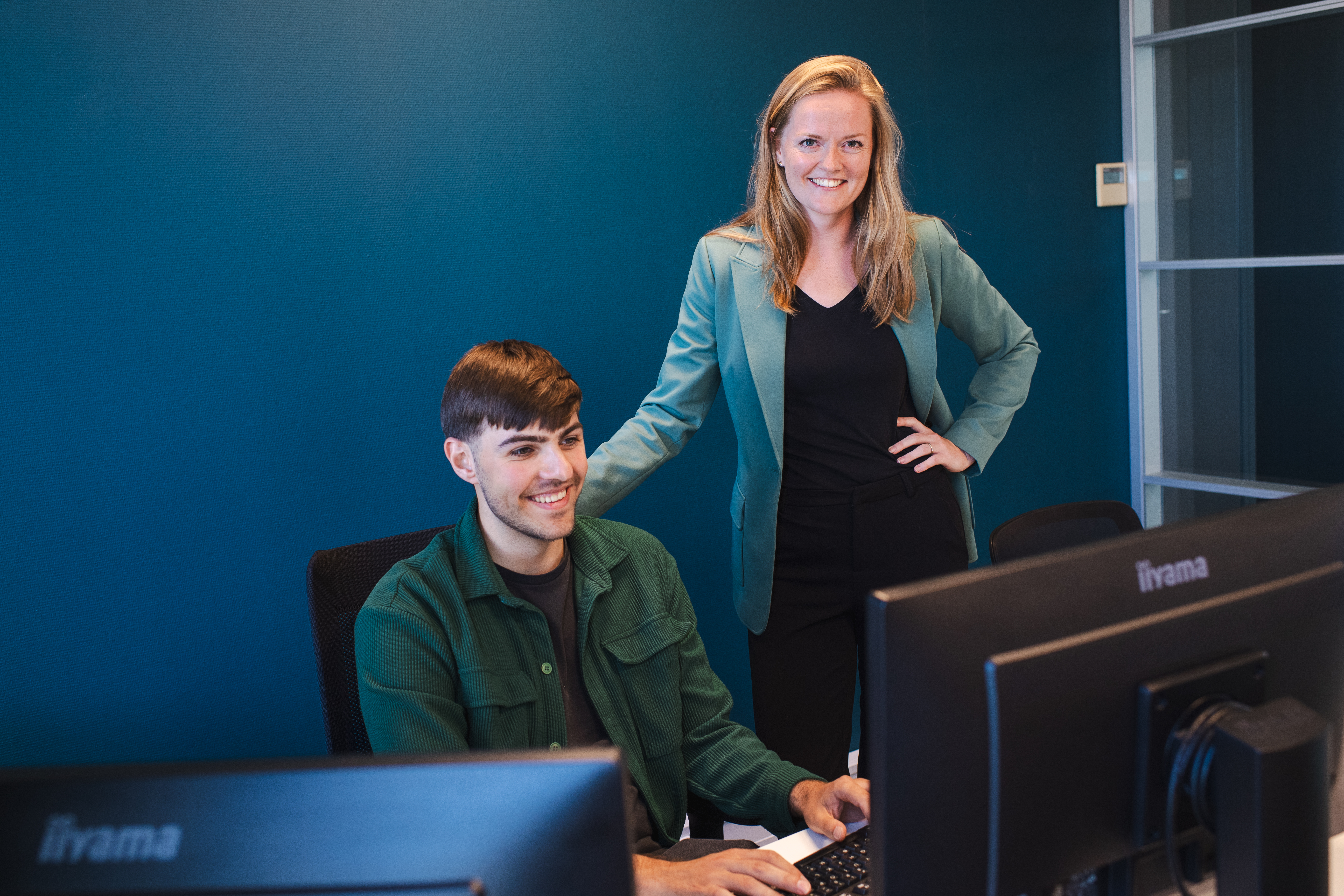 Persoon achter een computer, erachter staat een persoon die meekijkt.