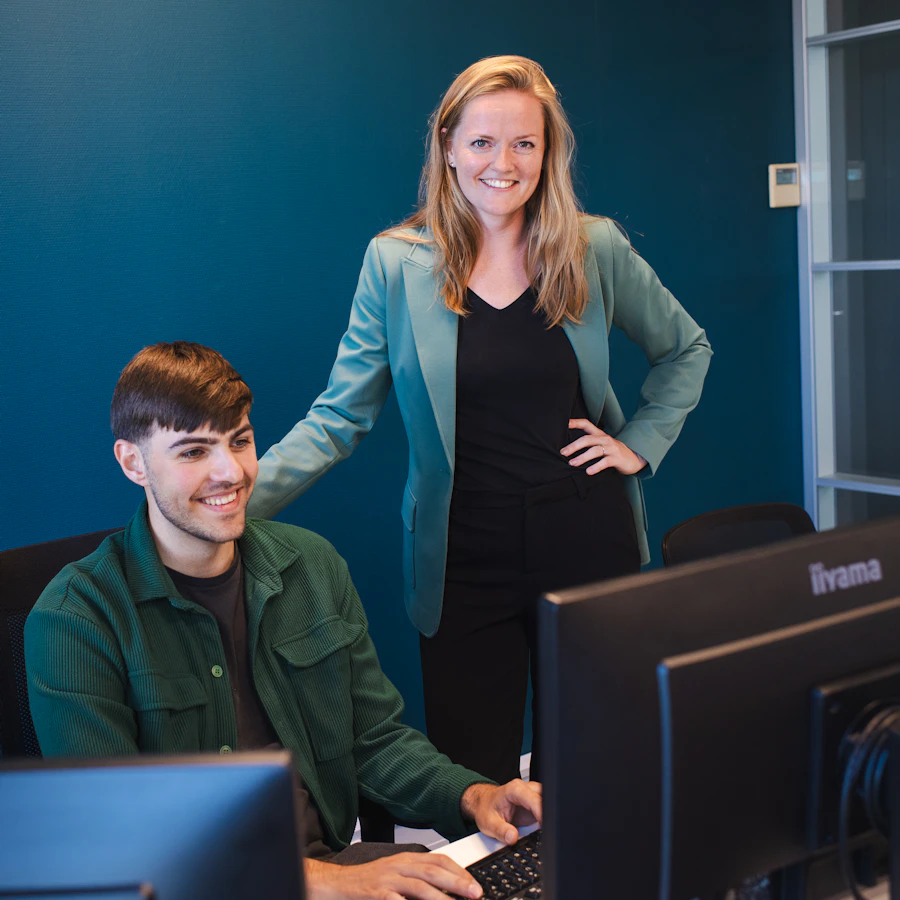 Persoon achter een computer, erachter staat een persoon die meekijkt.