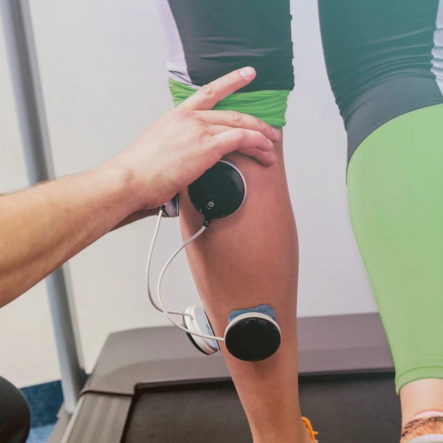 Patiënt op een loopband, fysiotherapeut plakt elektroden op kuiten van patiënt.