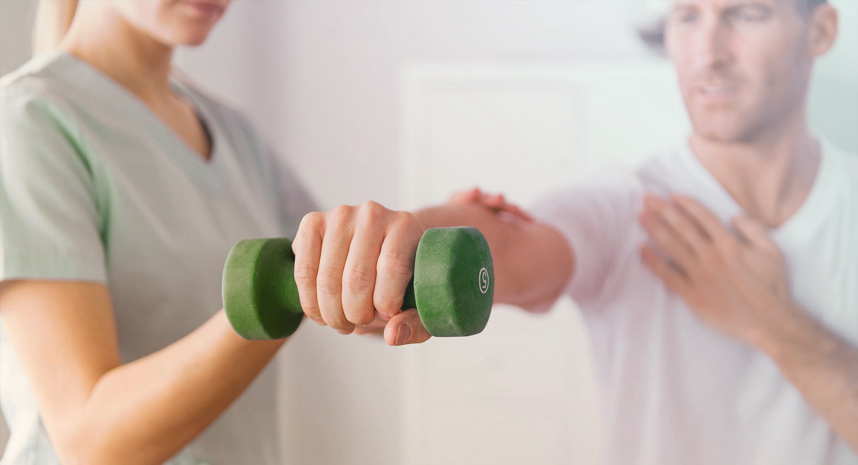 Persoon die met een hand een gewicht omhoog houdt, wordt ondersteund door een fysiotherapeut.