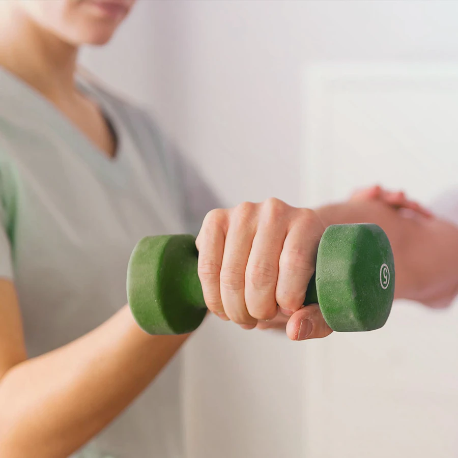 Persoon die met een hand een gewicht omhoog houdt, wordt ondersteund door een fysiotherapeut.