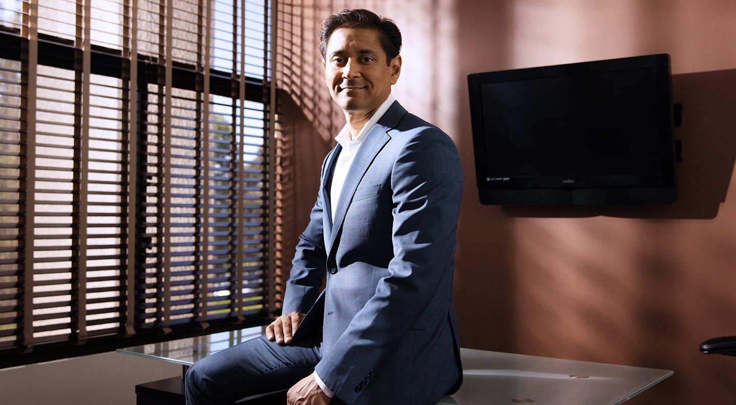 Dr. Savalia in suit sitting on Desk