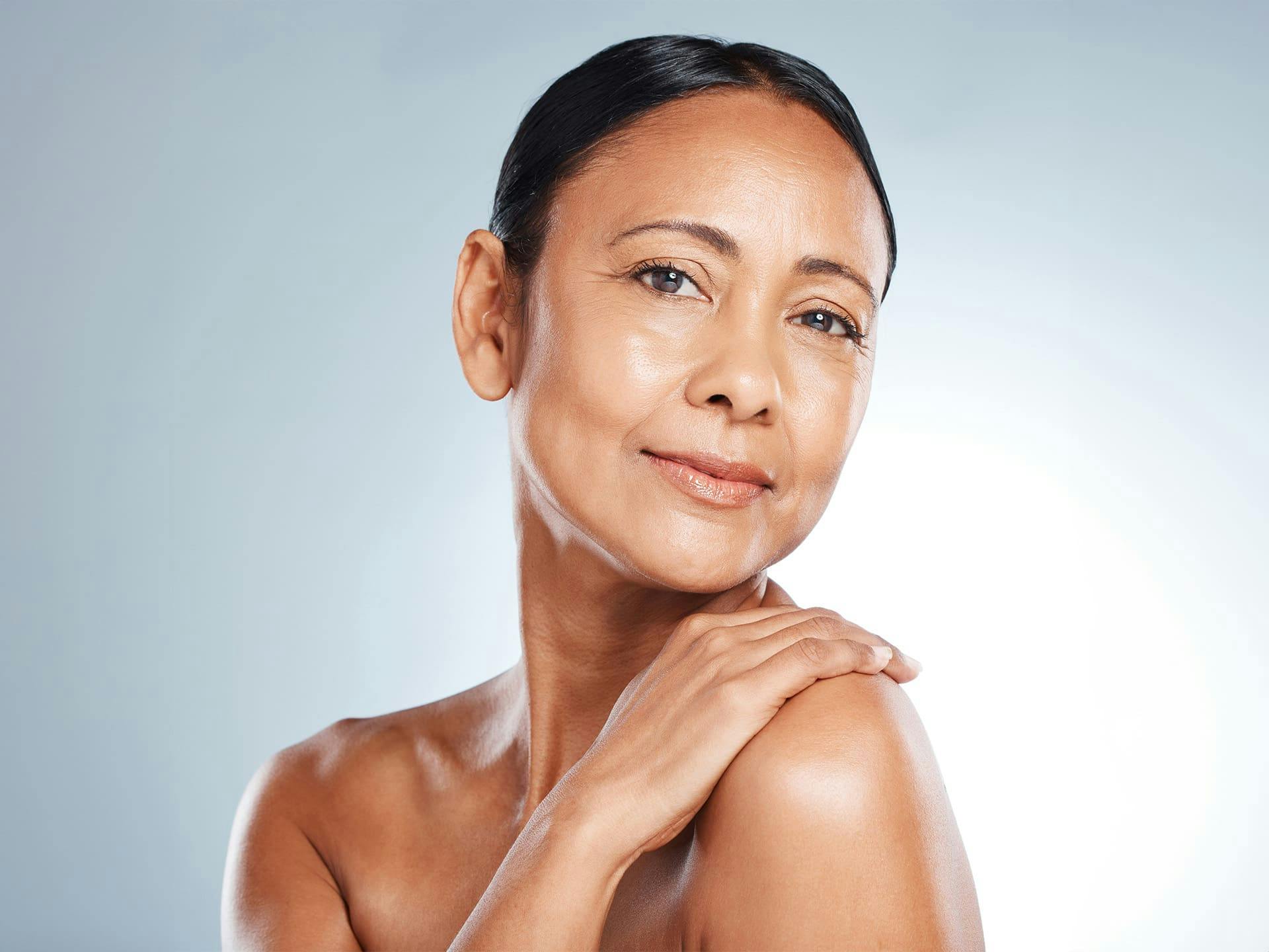 older woman with her hand on her shoulder with her hair tied back in a bun