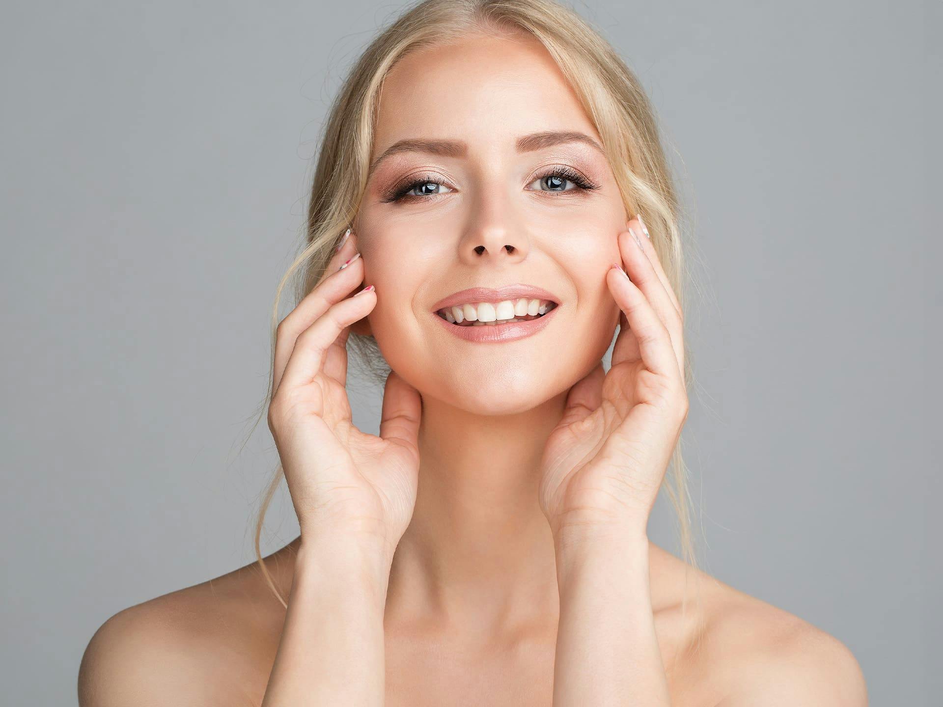 blonde woman looking forward, with her hands on her cheekbones