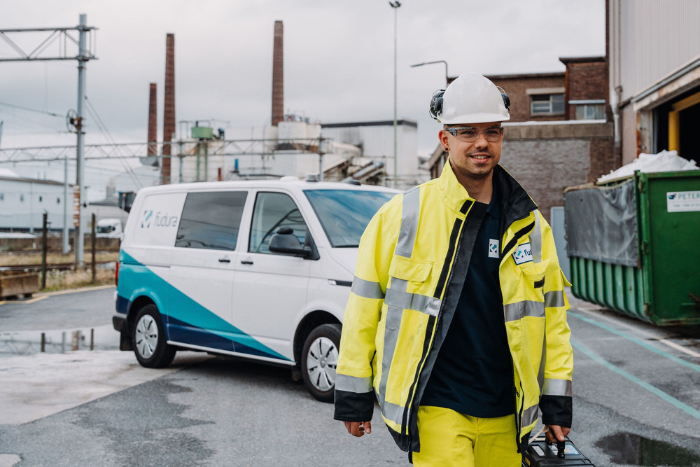 Persoon met een koffer loopt voor een fudura bus op een terrein