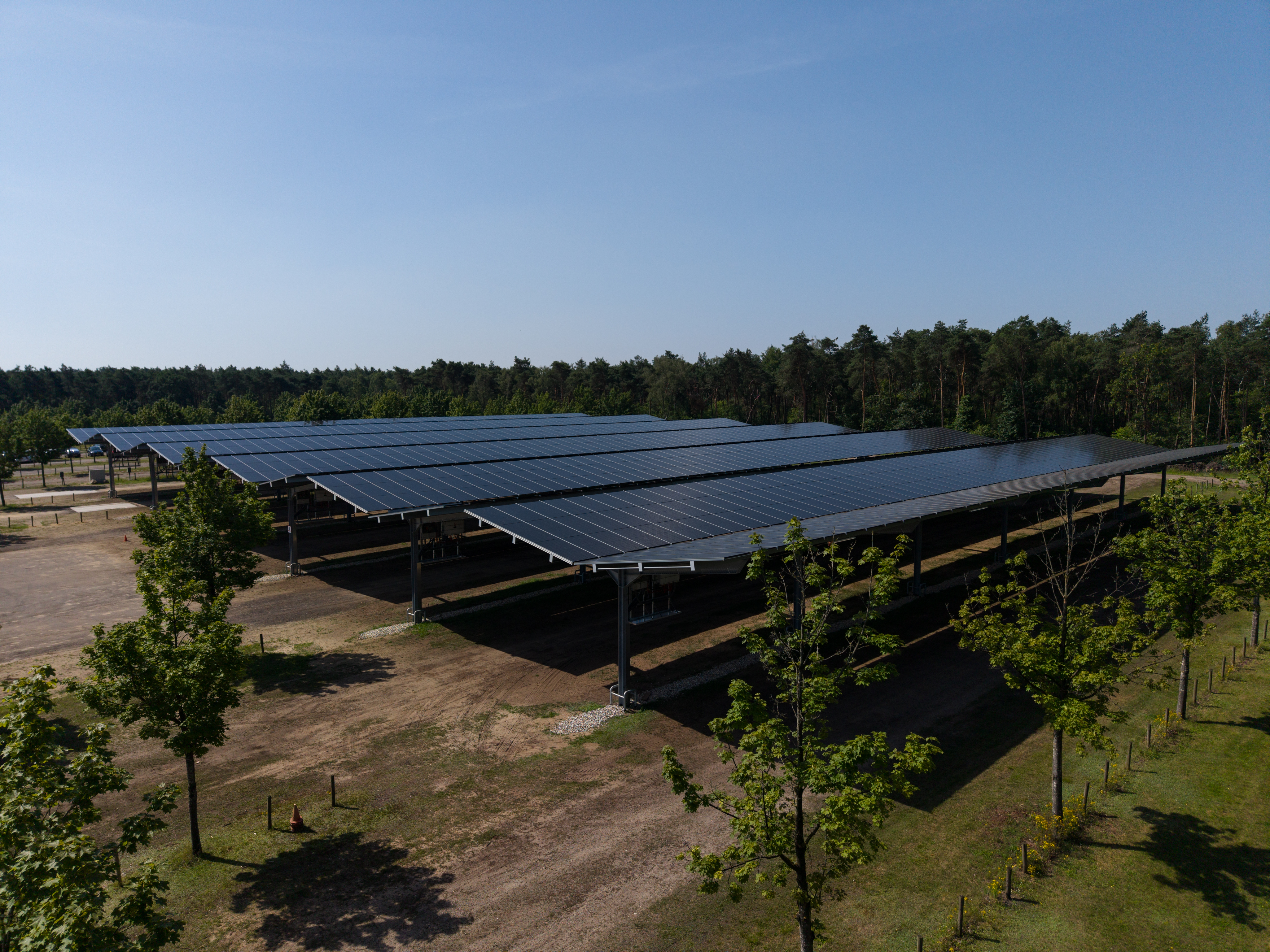 Luchtfoto van een smart solar carport van Fudura met zonnepanelen boven parkeerplaatsen, omgeven door bomen