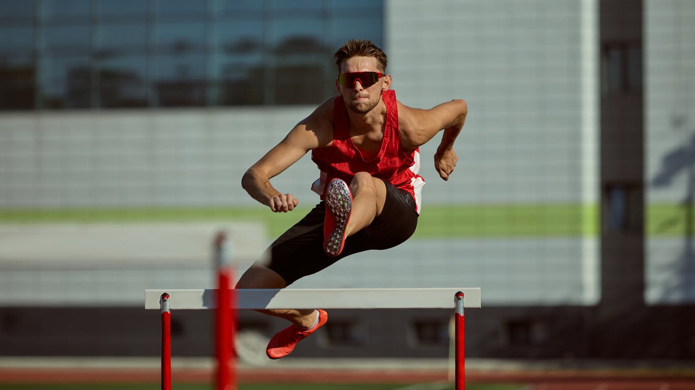 Male hurdler going over a hurdle about to hit his knee and tear the labral area in the hip