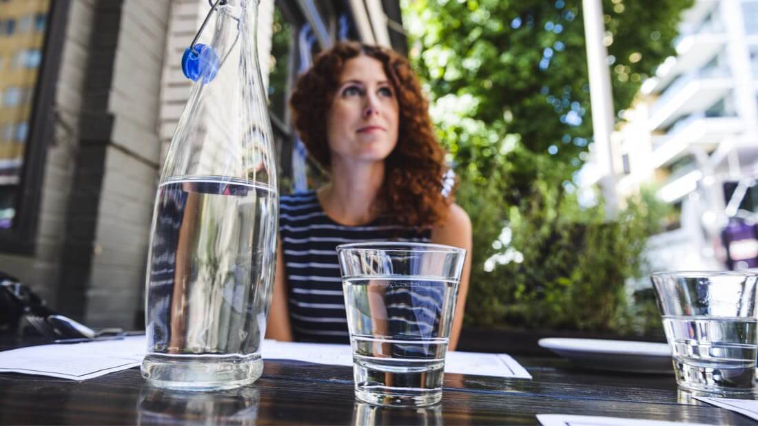 A woman sitting at an outside table with a glass of water