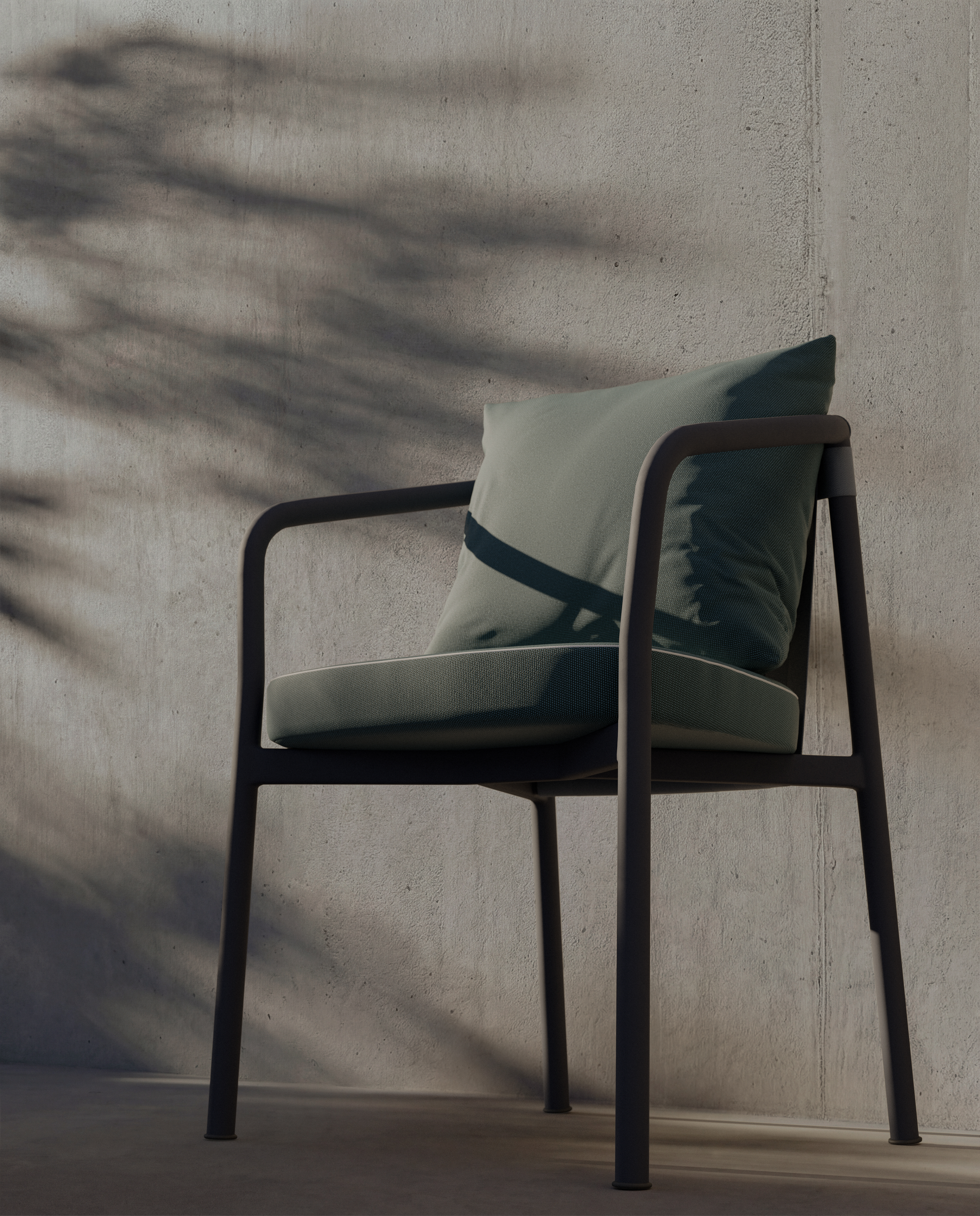 A modern chair with a green cushion and pillow sits against a concrete wall, with shadows of leaves and branches cast by sunlight across the wall and chair.