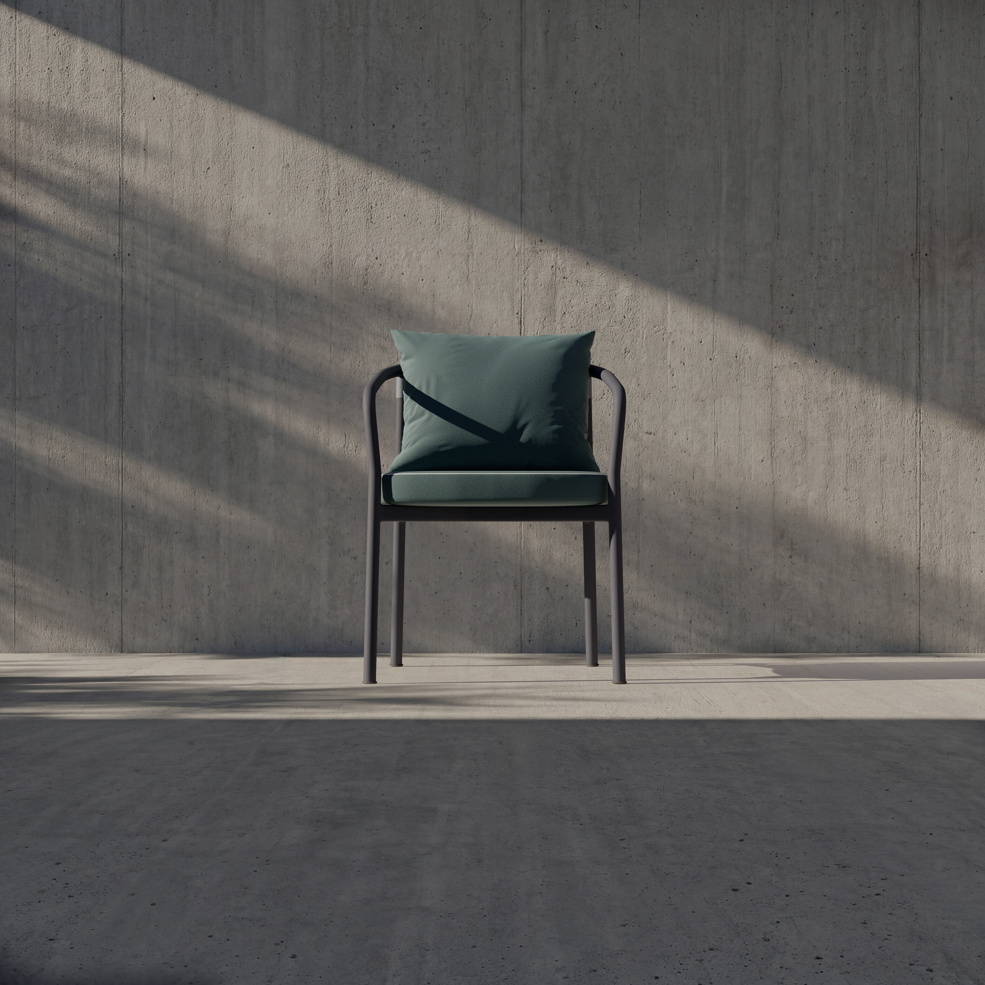 A modern black chair with a green cushion and matching pillow sits alone against a textured gray concrete wall, illuminated by angled sunlight casting shadows across the floor and wall.